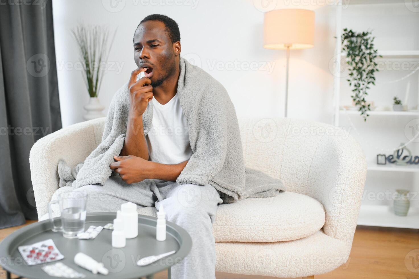 Sick african man using throat spray at home photo