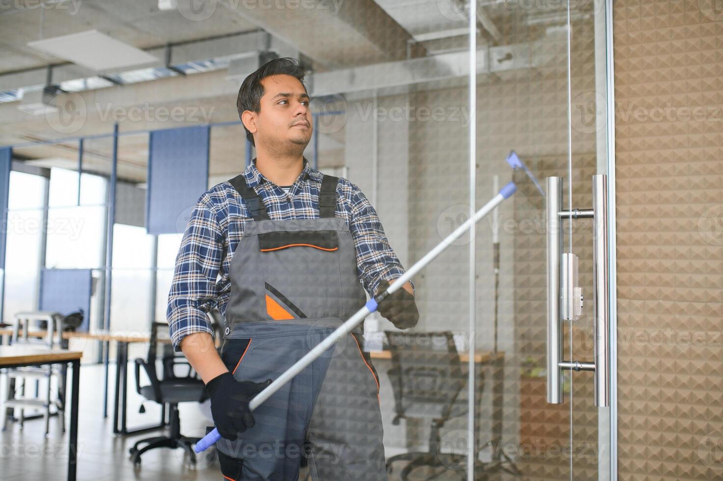 Male janitor cleaning window in office photo