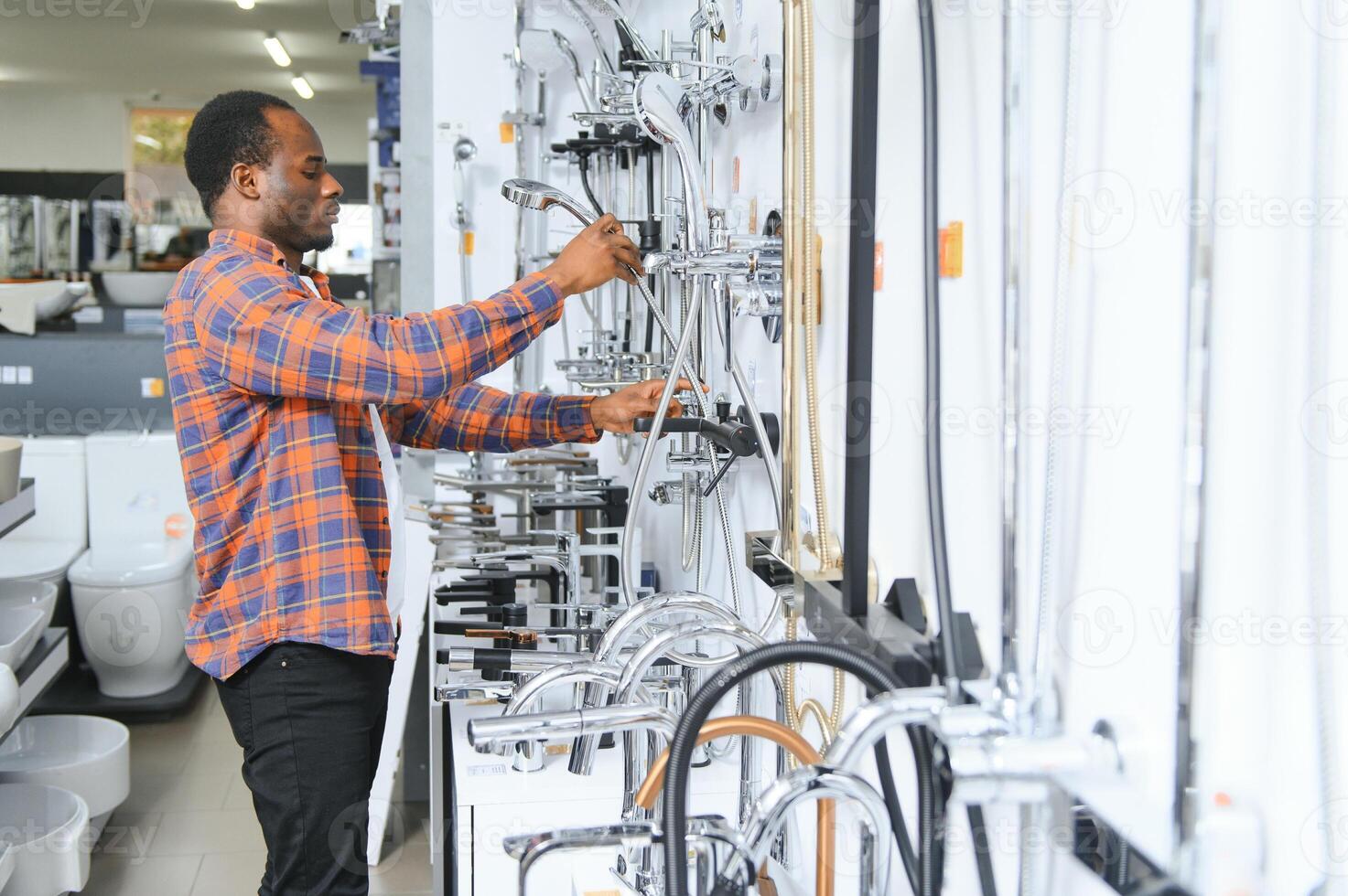 African man in a brown coat chooses a bathroom faucet in a construction supermarket, plumbing repairs in the house photo