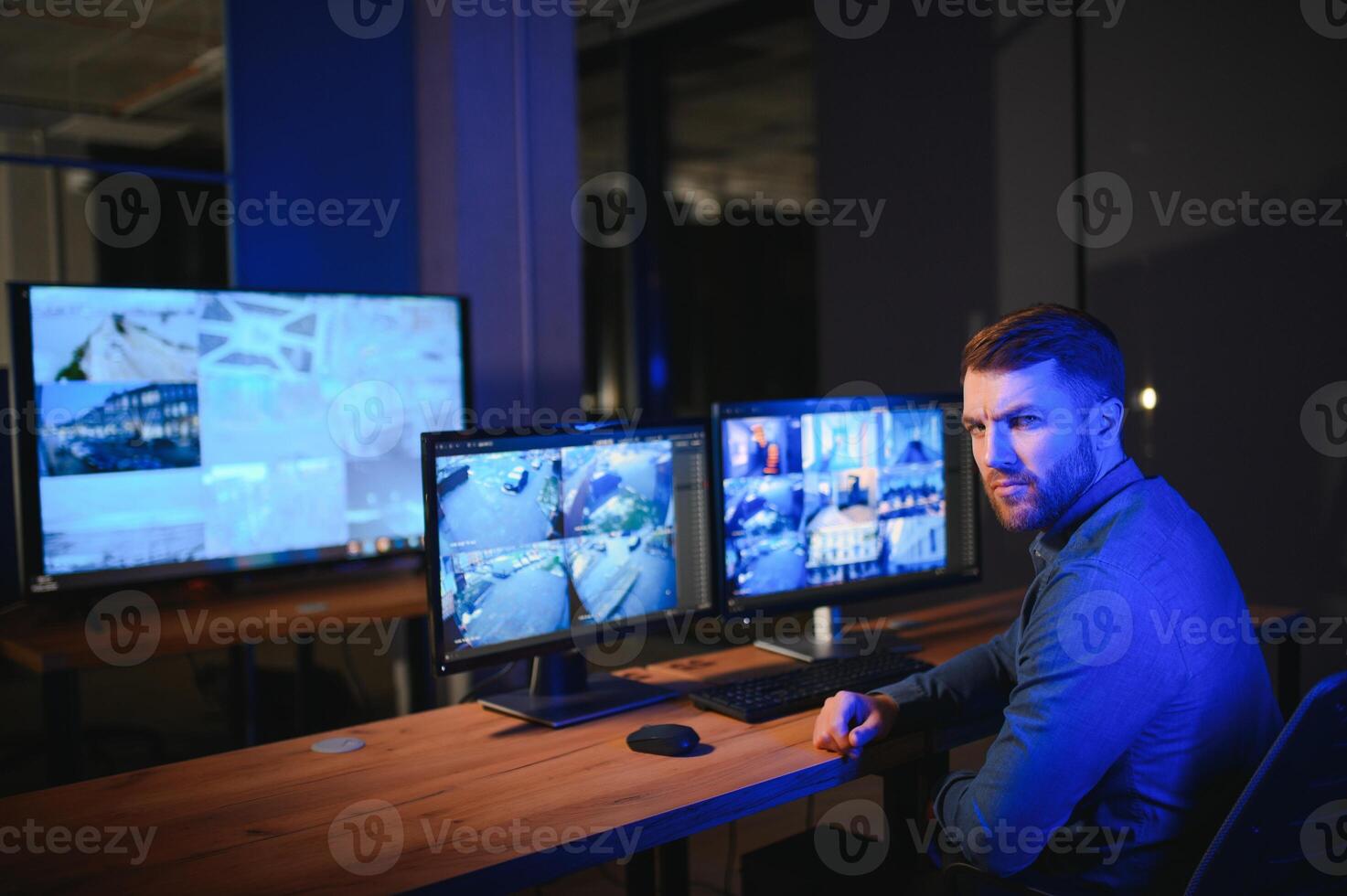 Rear view of security system operator looking at CCTV footage at desk in office photo