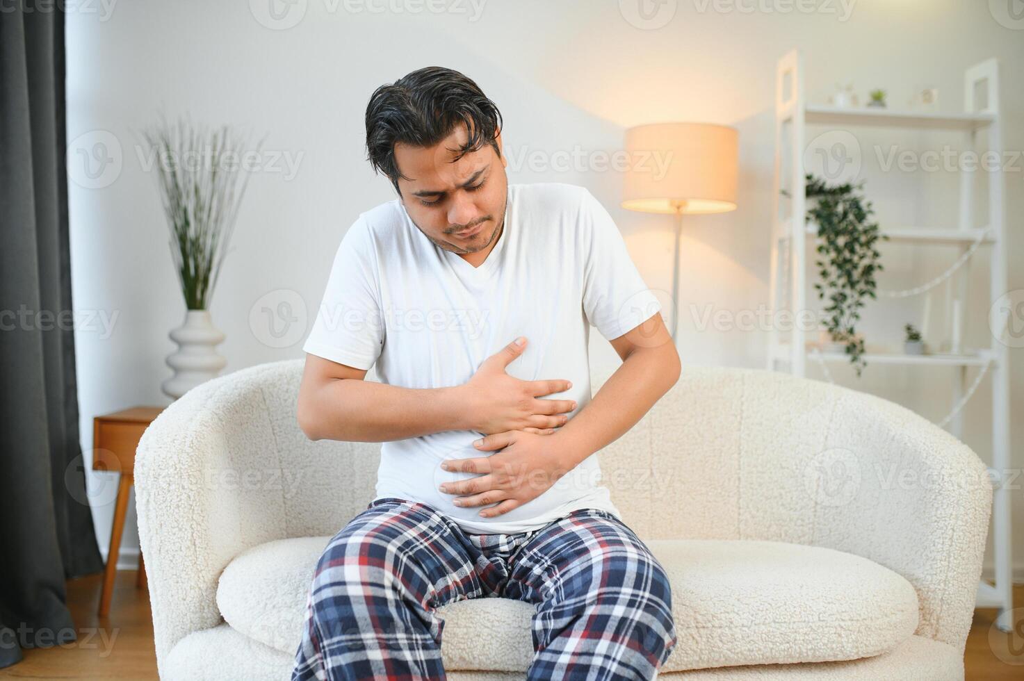 triste agotado chico de indio y árabe etnicidad, sostiene su manos en su estómago, muecas desde dolor en su estómago, sufre desde envenenamiento, espasmo, estómago problemas foto