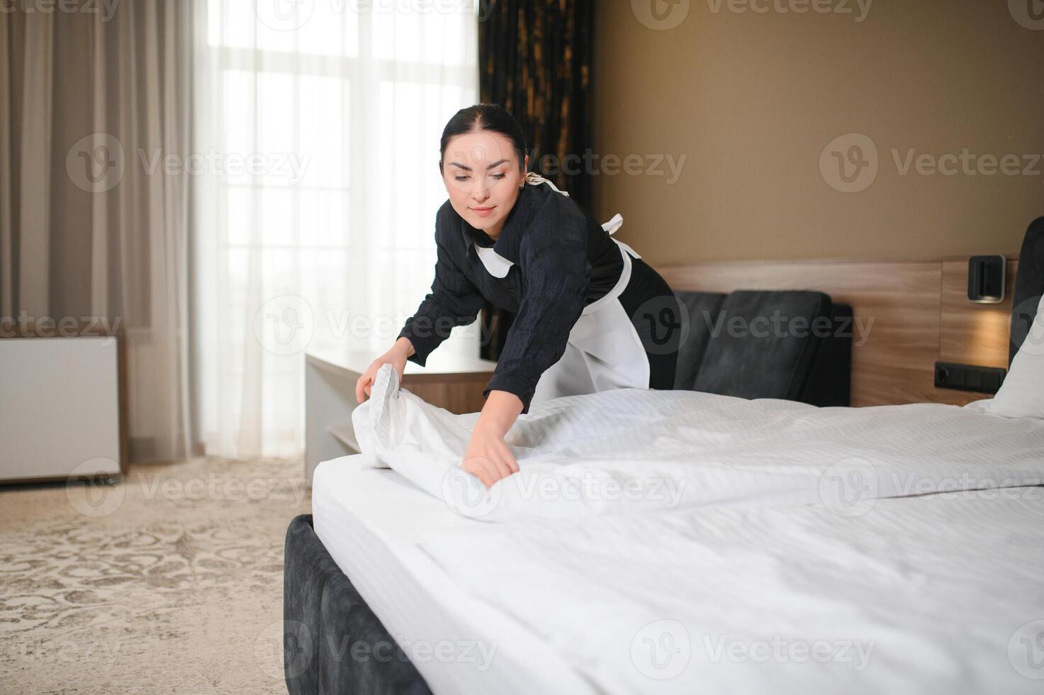 Young maid making bed in hotel room photo