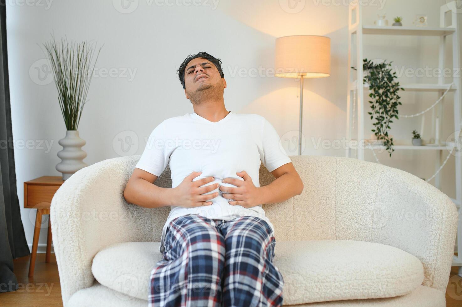 Sad exhausted guy of indian and arabian ethnicity, holds his hands on his stomach, grimaces from pain in his stomach, suffers from poisoning, spasm, stomach problems photo