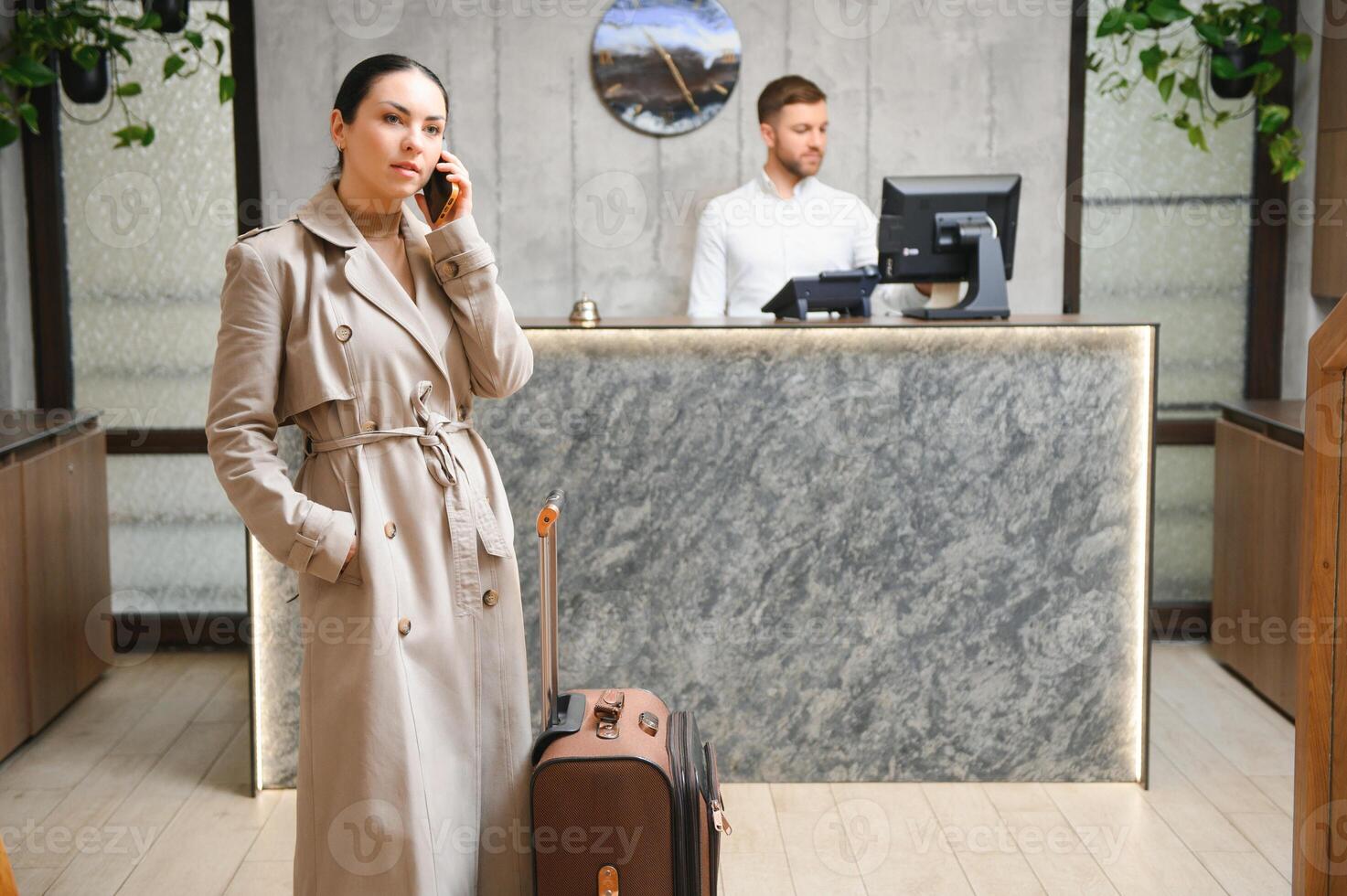 Businesswoman with luggage in modern hotel lobby using smartphone photo