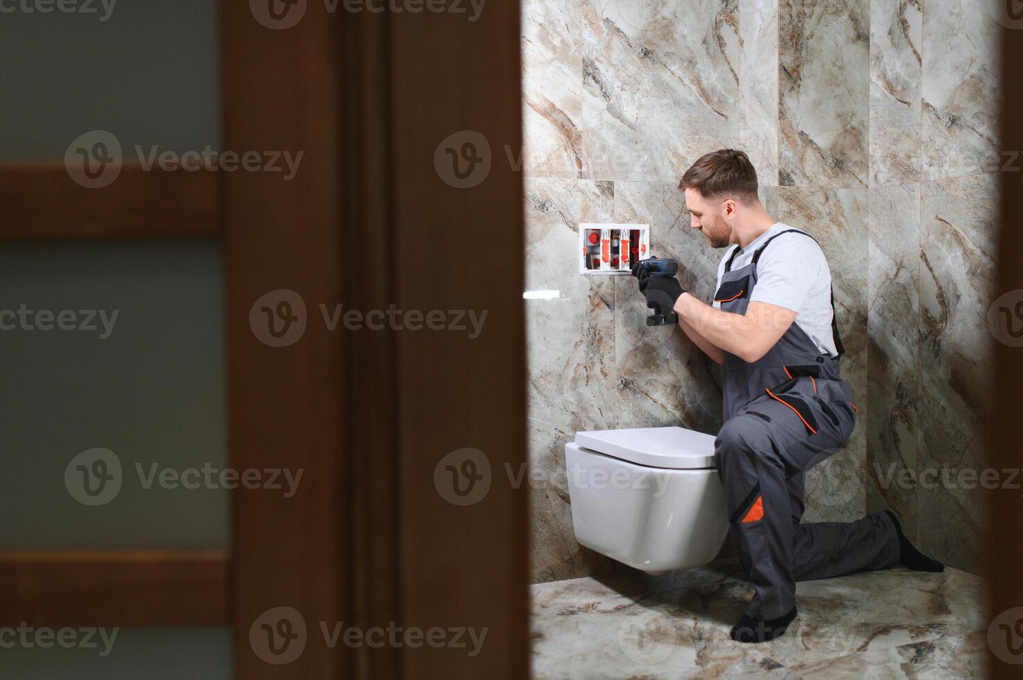 Professional plumber working with toilet bowl in bathroom photo