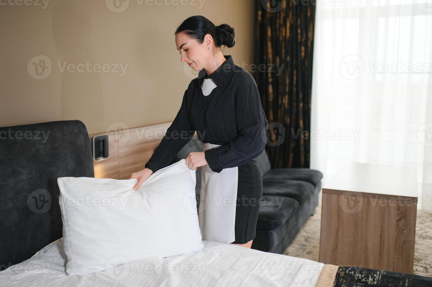 Young maid making bed in hotel room photo