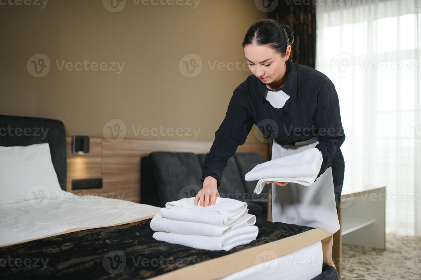 Housemaid making bed in hotel room while folding towels photo