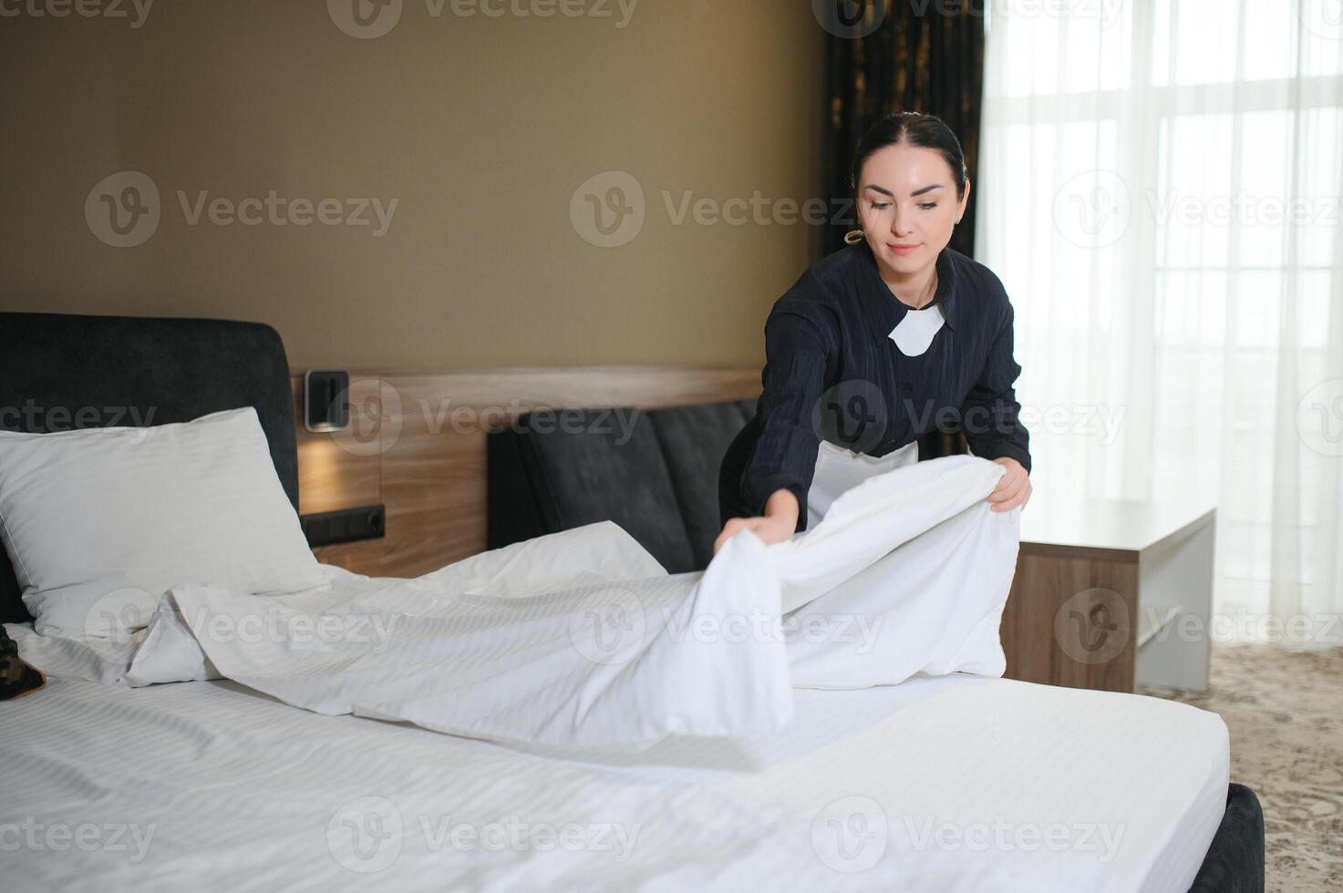 Young maid making bed in hotel room photo