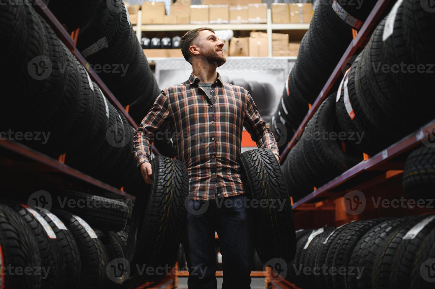 Glad male customer taking new tires in the supermarket for buying. He looks happy. Big shopping mall with car goods photo