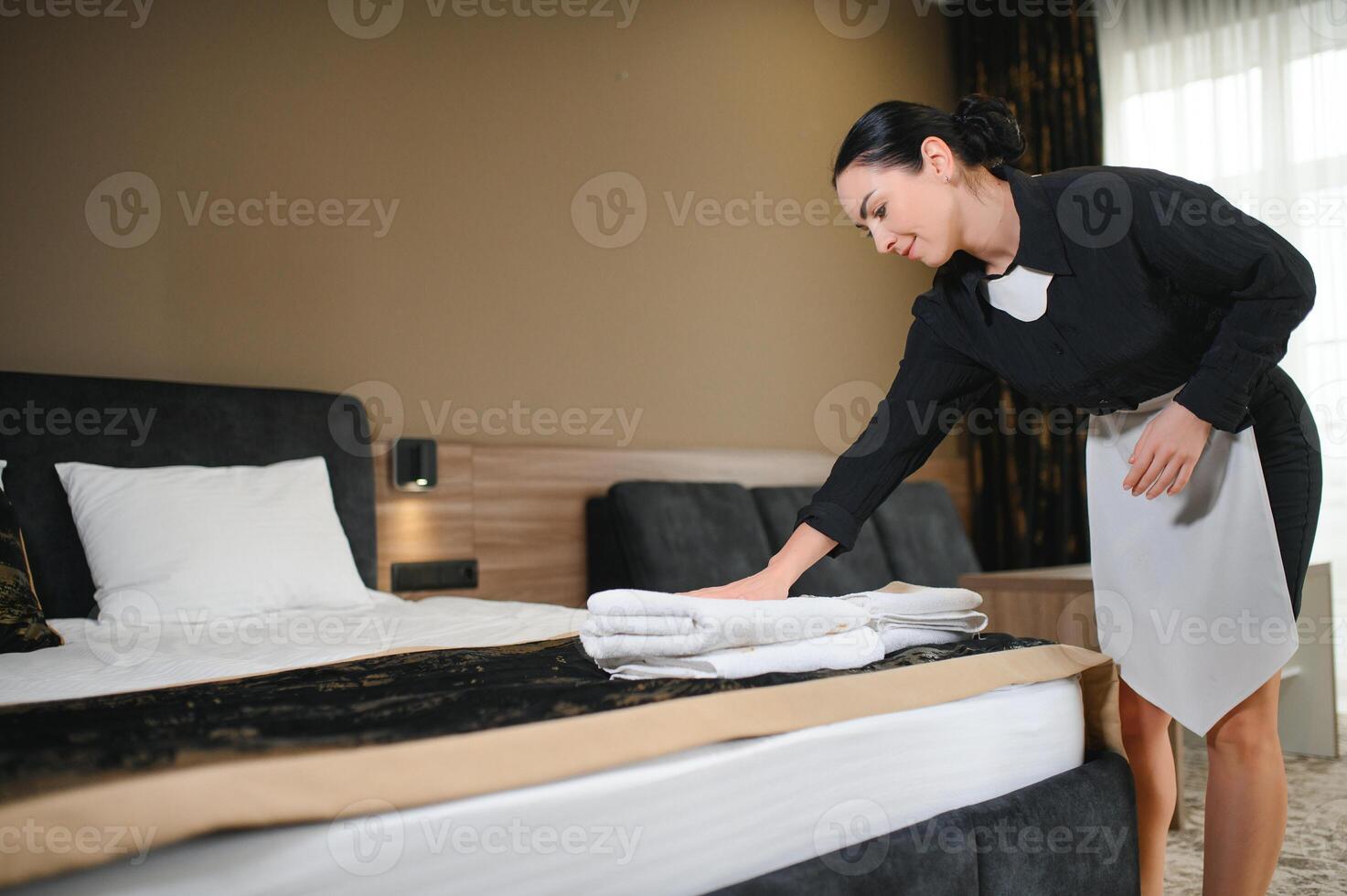 Maid holding fresh towels with flowers in hotel room photo