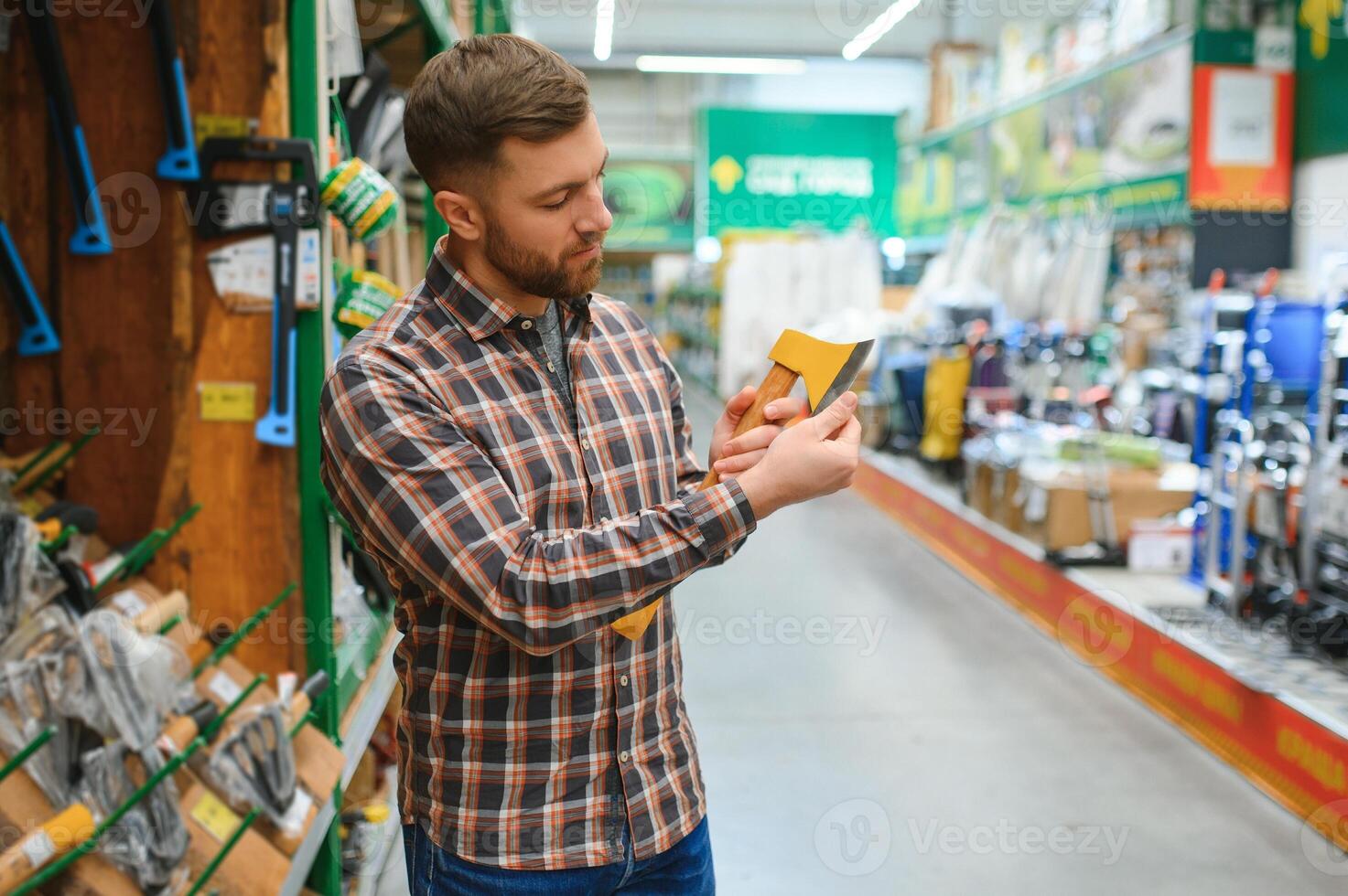 A young man chooses axe in the hardware store photo