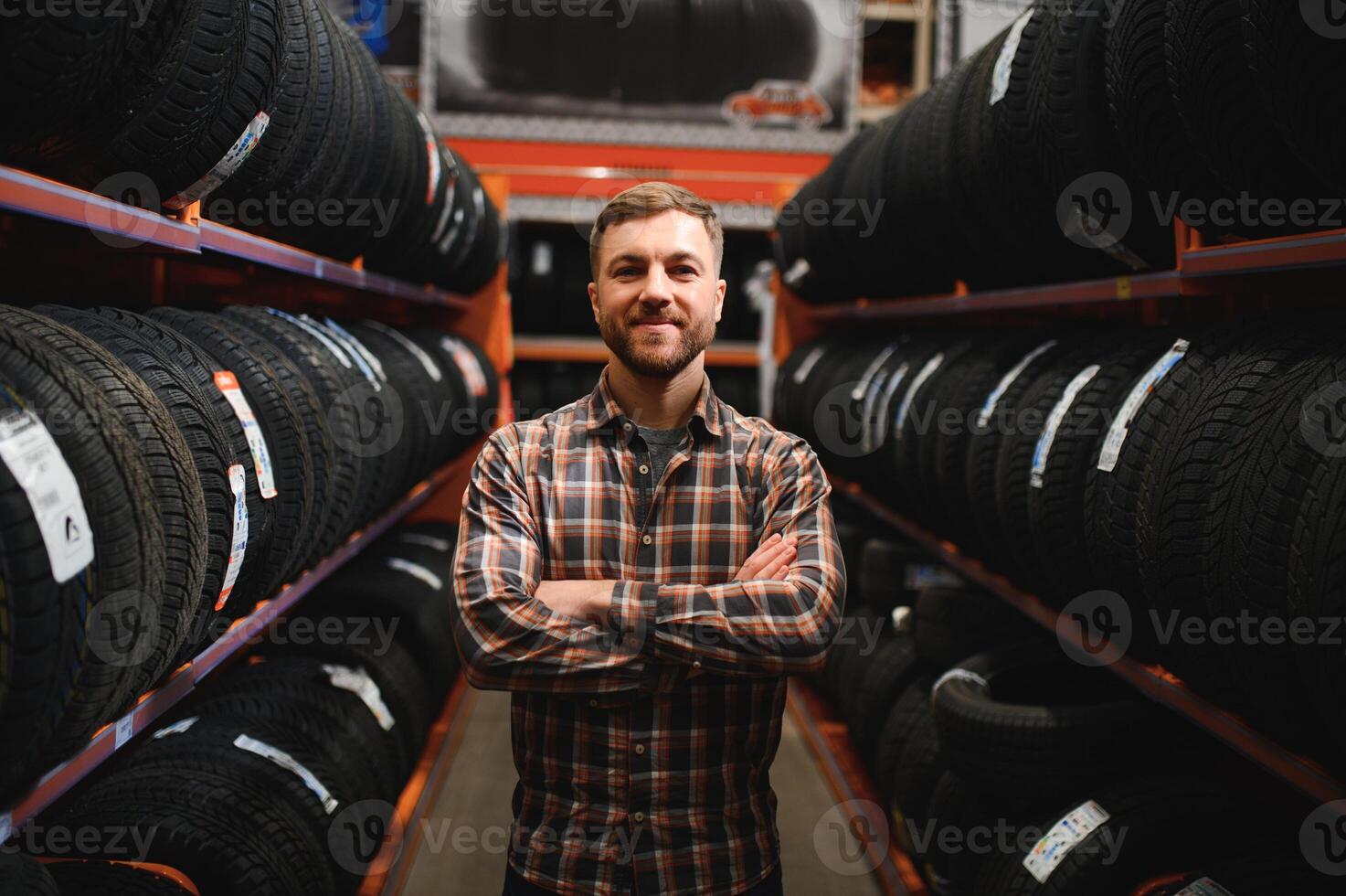 Glad male customer taking new tires in the supermarket for buying. He looks happy. Big shopping mall with car goods photo