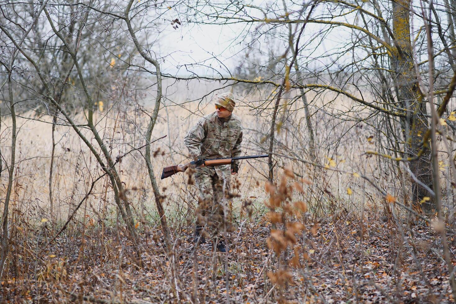 hunting, war, army and people concept - young soldier, ranger or hunter with gun walking in forest. photo