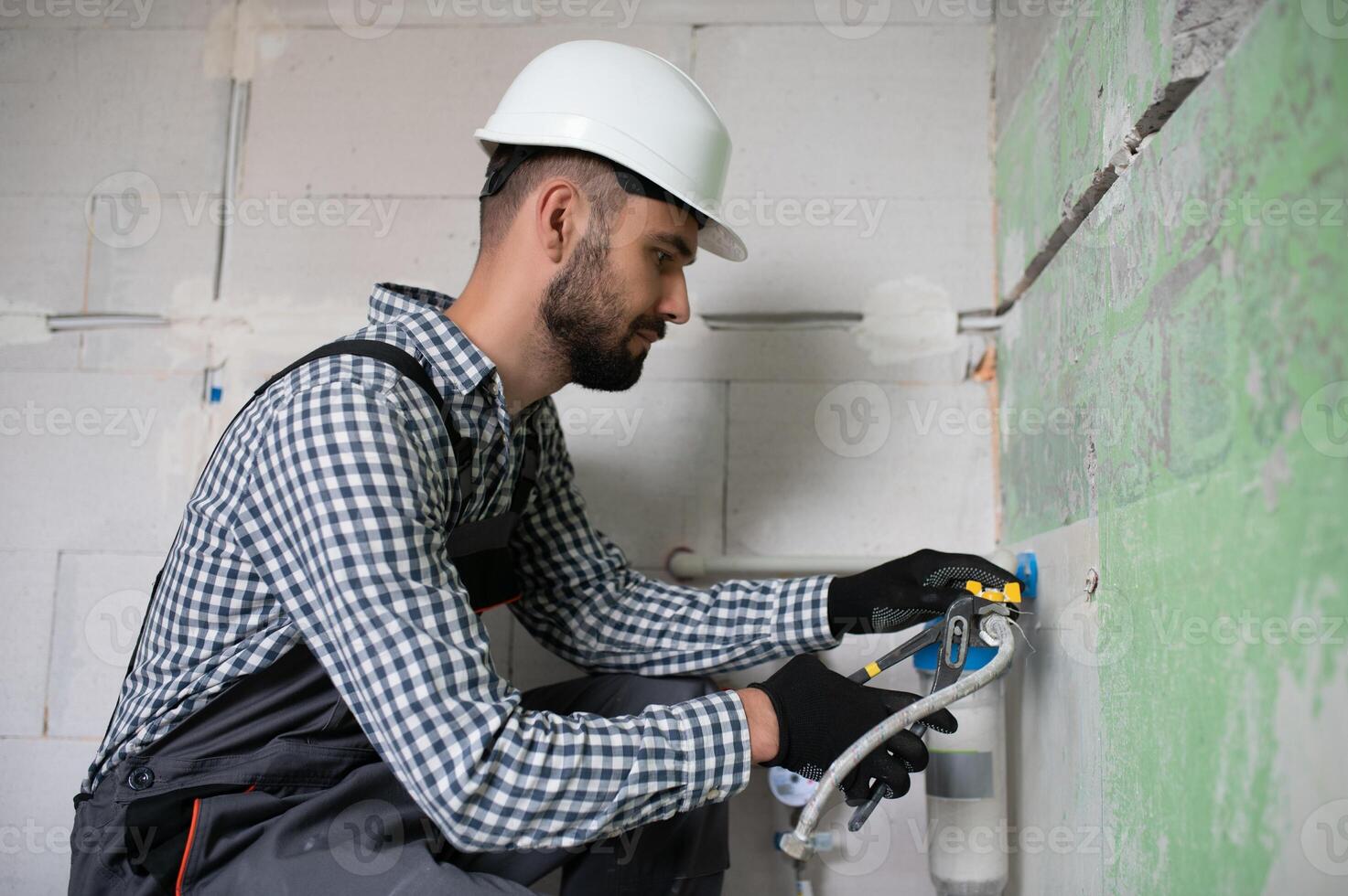 Horizontal snapshot of young plumber working with grey sewer pipes, fixing them to wall with a help of screwdriver. photo