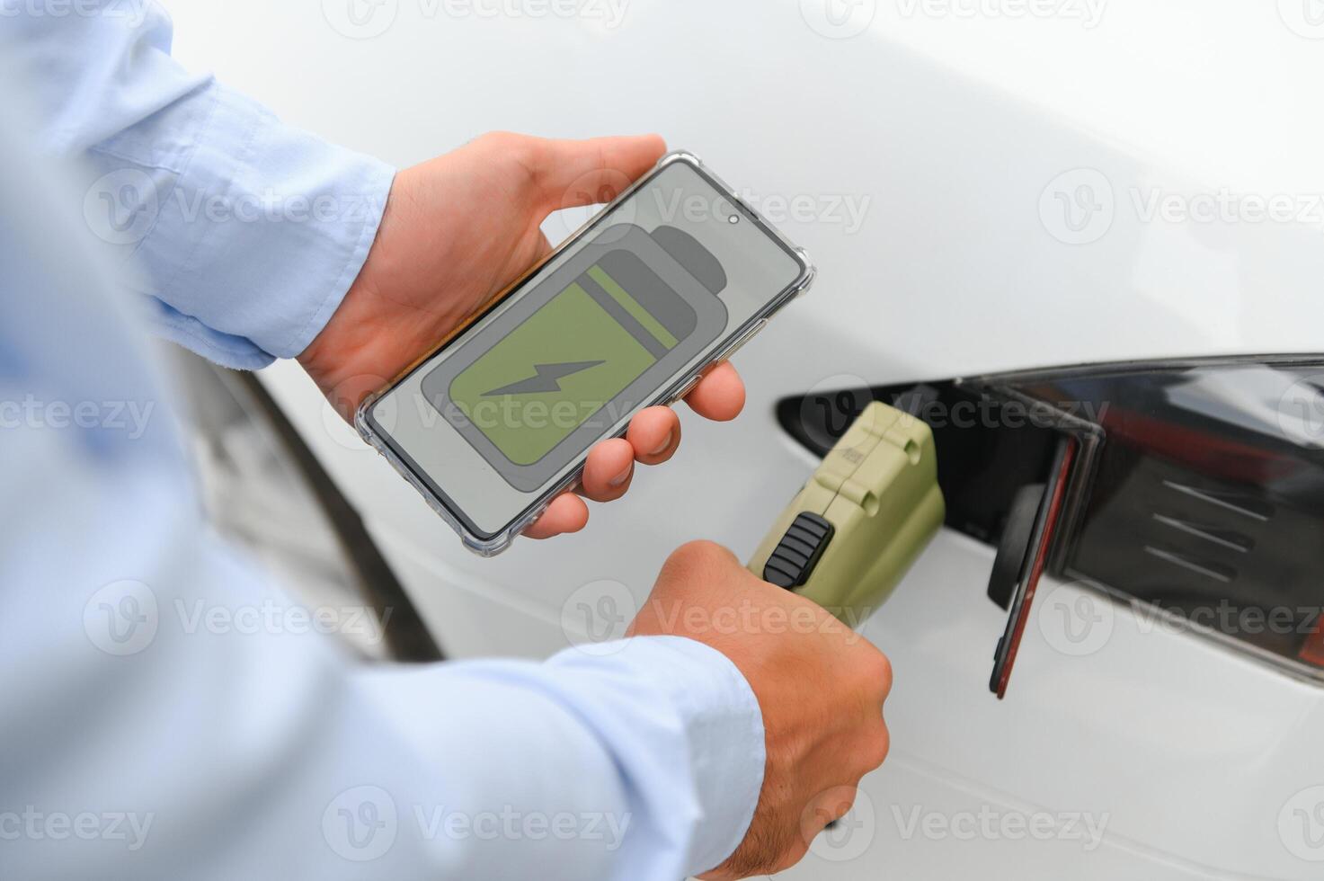 Happy man using smart phone and charging car at vehicle charging station photo