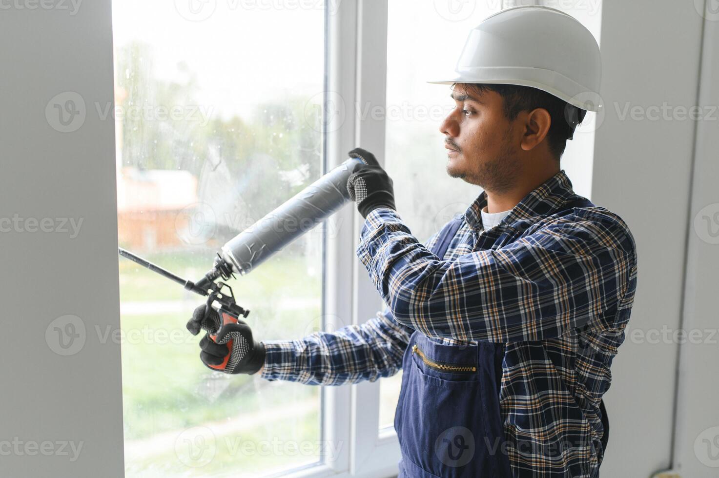 indio trabajador utilizando un silicona tubo para reparando de ventana interior foto