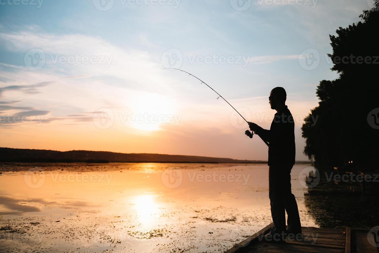 Fisher man fishing with spinning rod on a river bank at misty foggy sunrise. fisher with spinning. spinning concept. photo