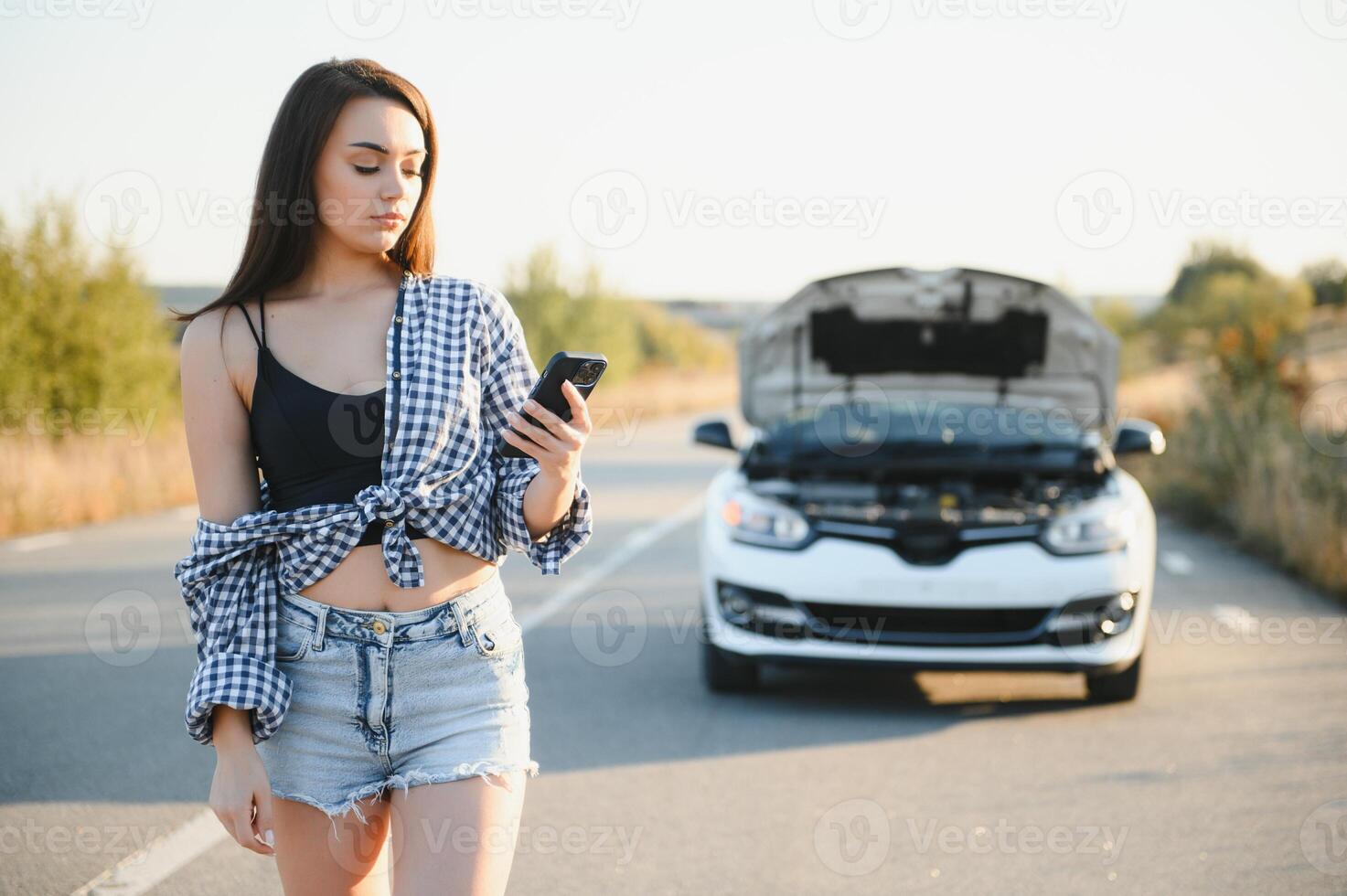el joven niña rompió el coche y ella abrió el capucha y intentó a reparar el coche en el la carretera. un mujer llamadas en un teléfono inteligente con un coche evacuación Servicio foto
