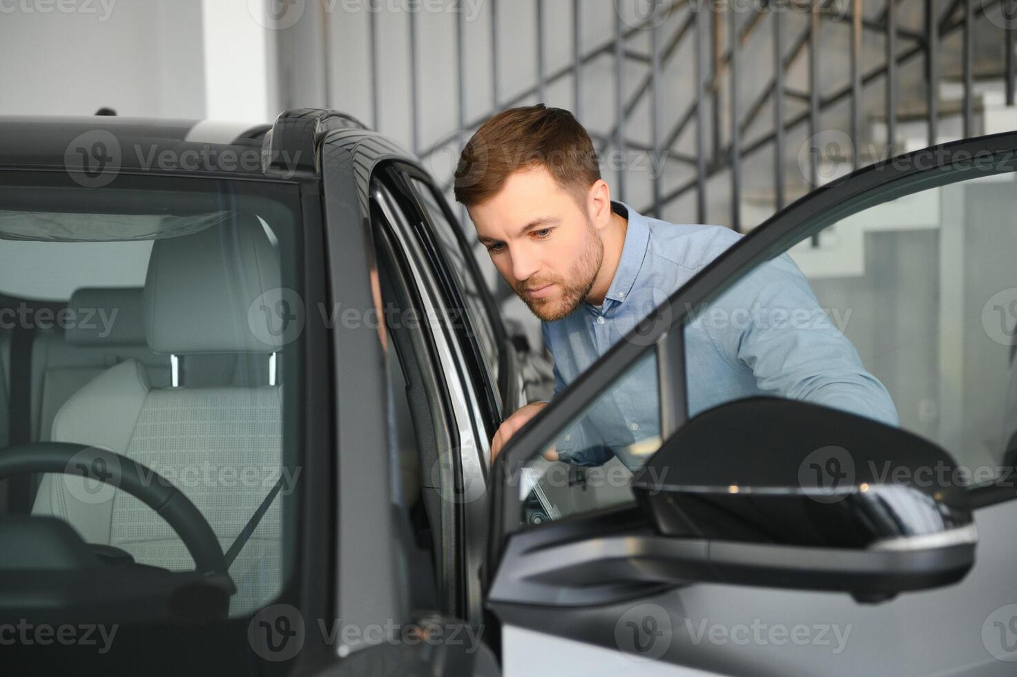Young man, selling electric cars in the showroom. Concept of buying eco-friendly car for family photo