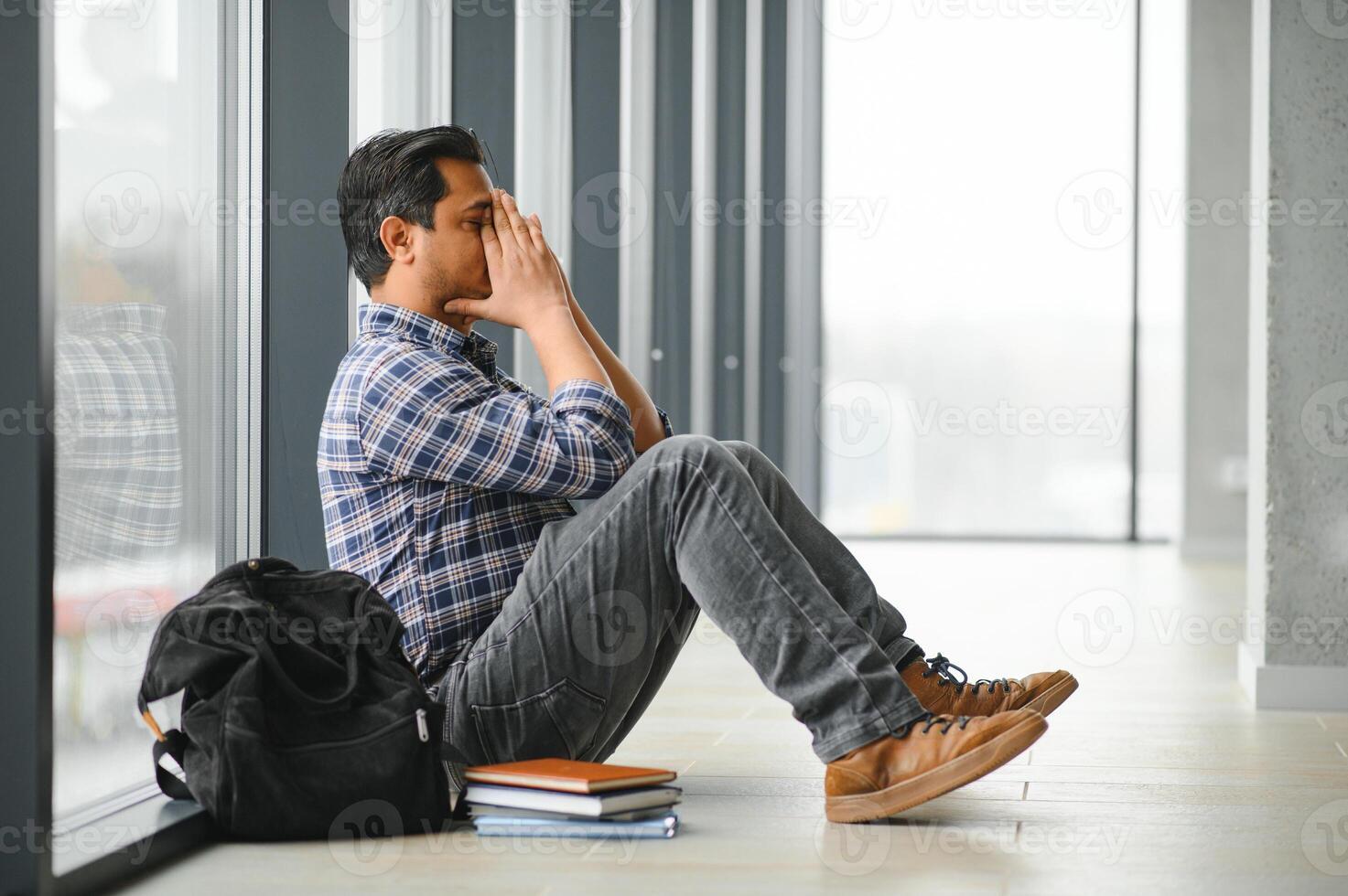 Full length of depressed boy sitting with backpack in school corridor photo