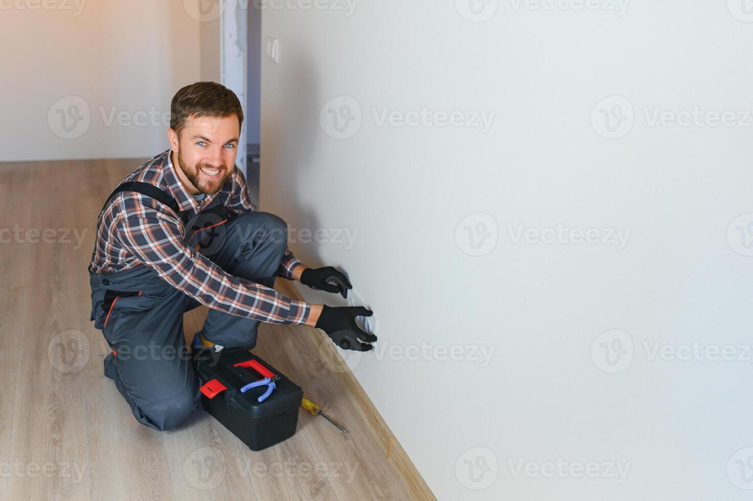 confidente profesional electricista en uniforme utilizando destornillador mientras reemplazando un enchufe en Departamento después renovación trabajar. foto