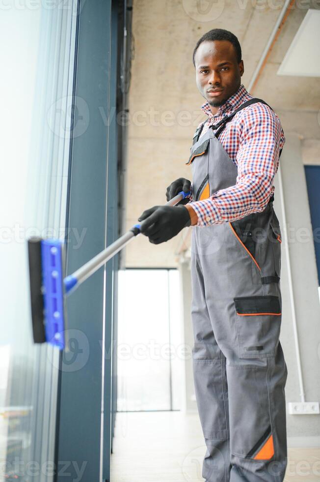 worker of cleaning organization carefully and carefully rubs large window of the office space. A serious African-American in blue overalls wipes the double-glazed window in the office photo