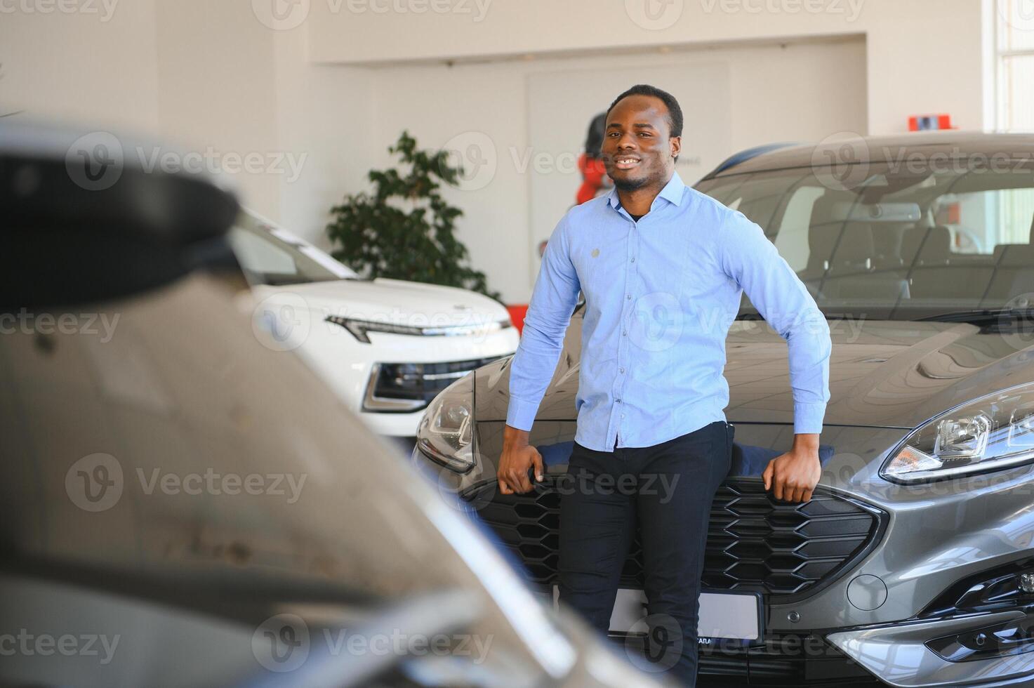 su sueño coche. contento joven africano hombre mirando emocionado elegir un coche a el concesión foto