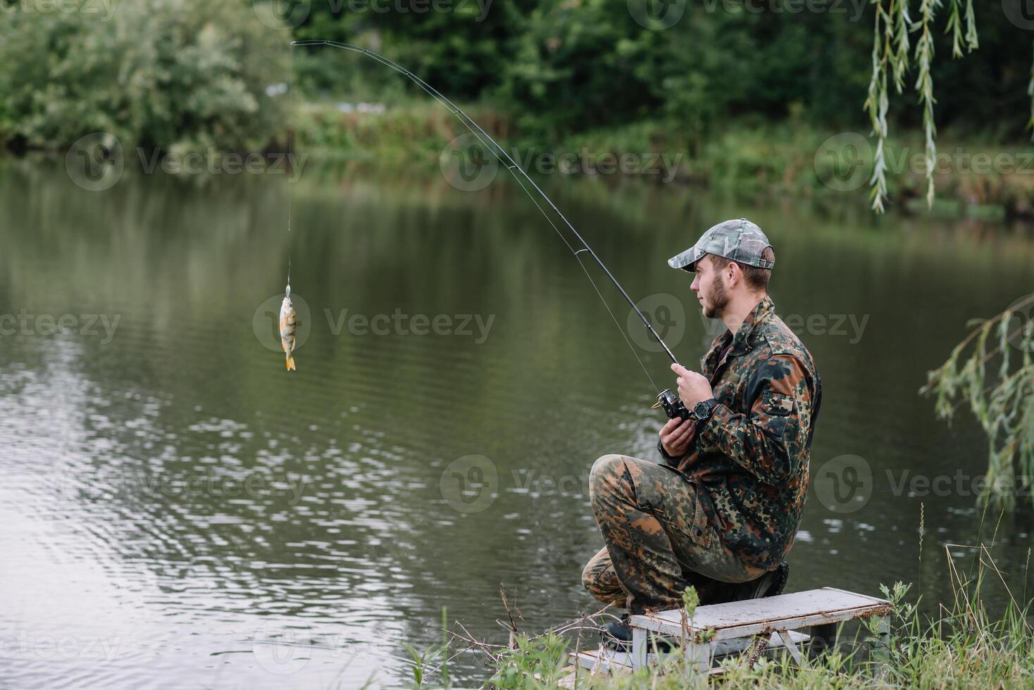 pescar en rio.a pescador con un pescar varilla en el río banco. hombre pescador capturas un pescado pesca del lucio, hilado carrete, pez, breg ríos - el concepto de un rural escapar. artículo acerca de pescar foto