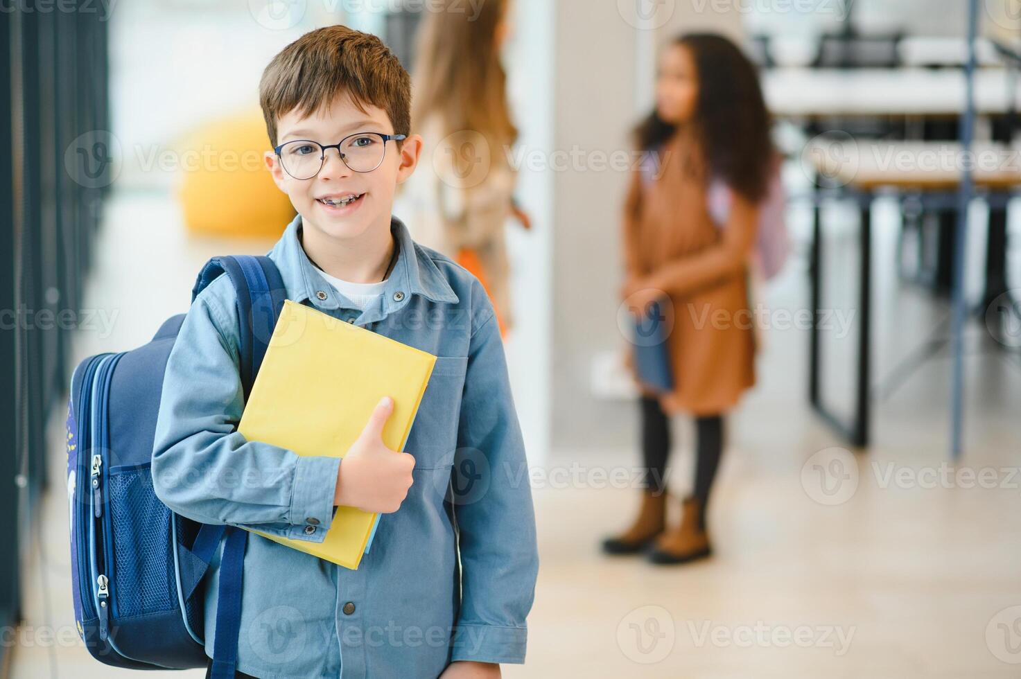 Happy cute clever boy in glasses with school bag and book in his hand photo