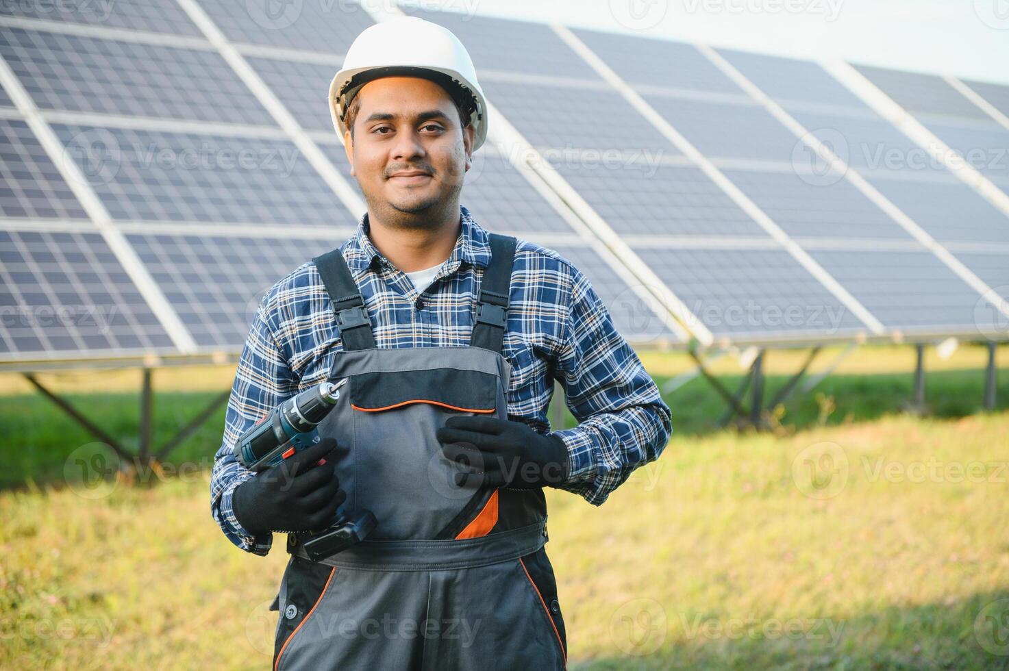 An Indian worker in uniform and with tools works on a solar panel farm photo