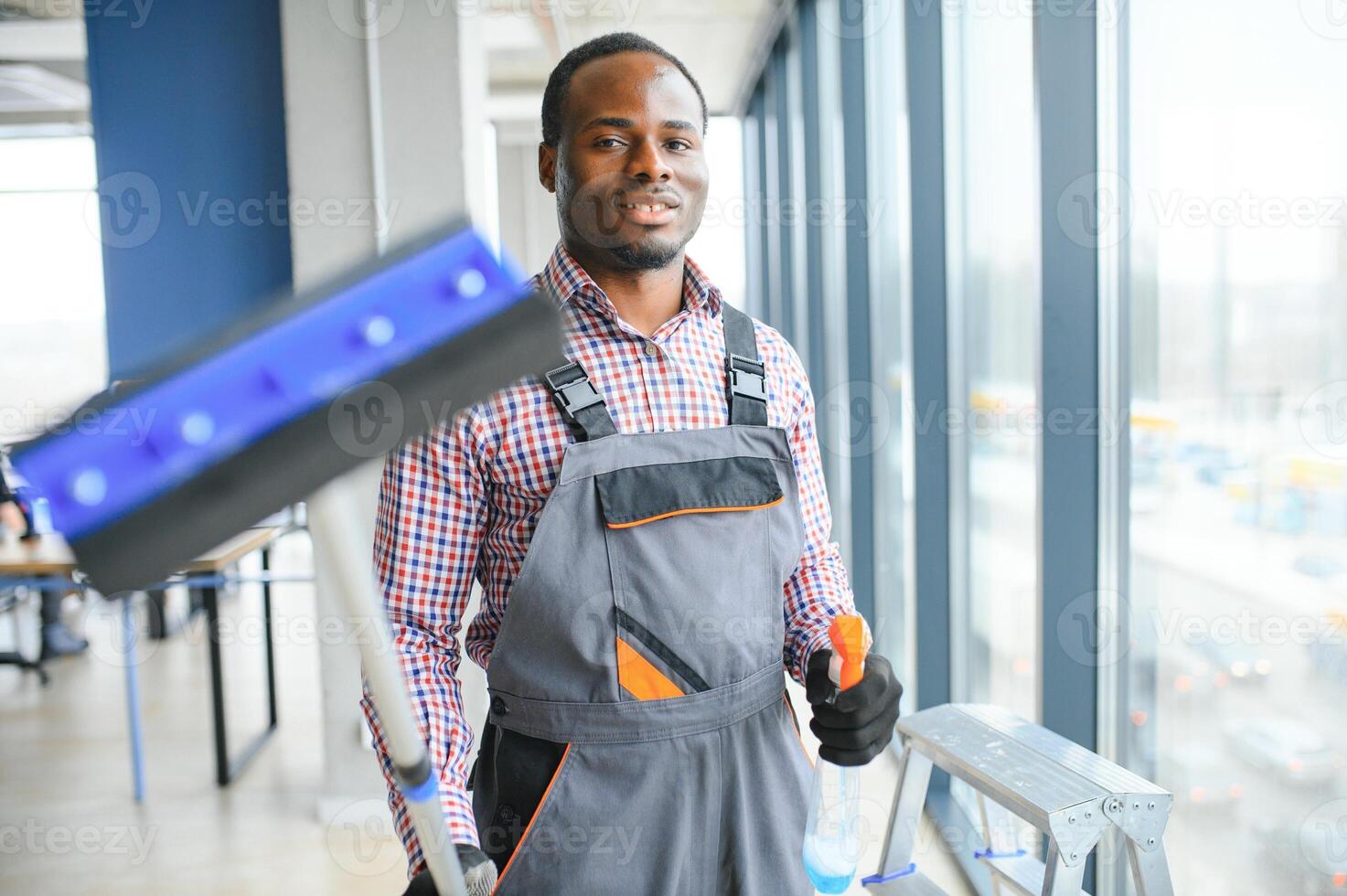 worker of cleaning organization carefully and carefully rubs large window of the office space. A serious African-American in blue overalls wipes the double-glazed window in the office photo