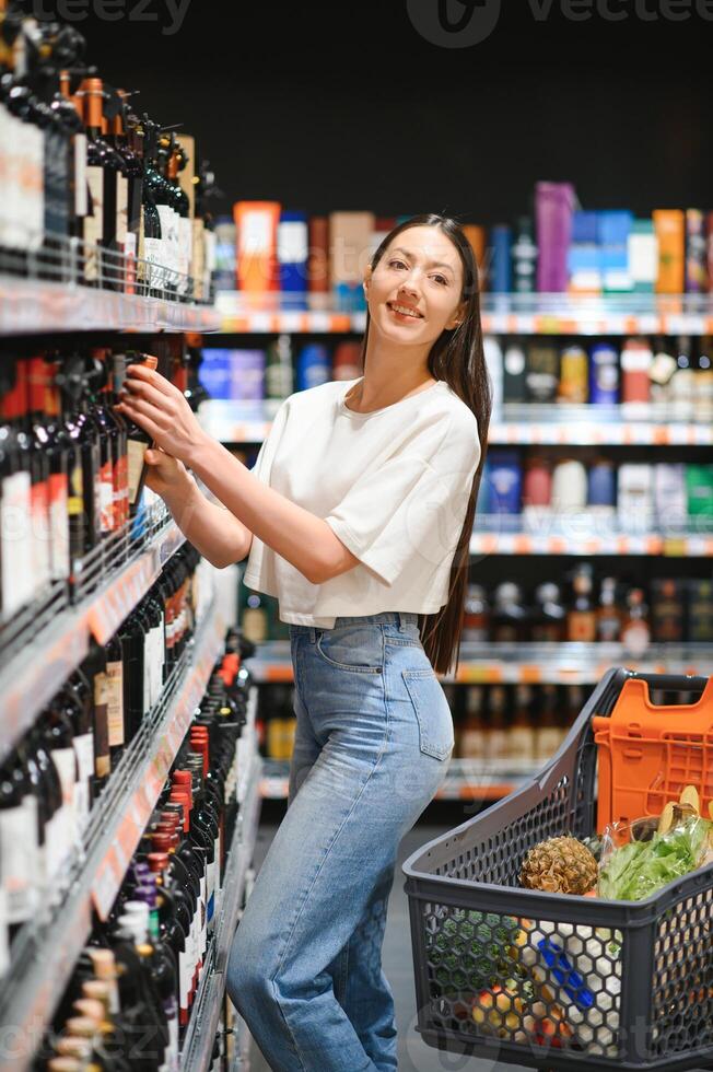 joven mujer decidiendo qué vino a comprar en supermercado foto