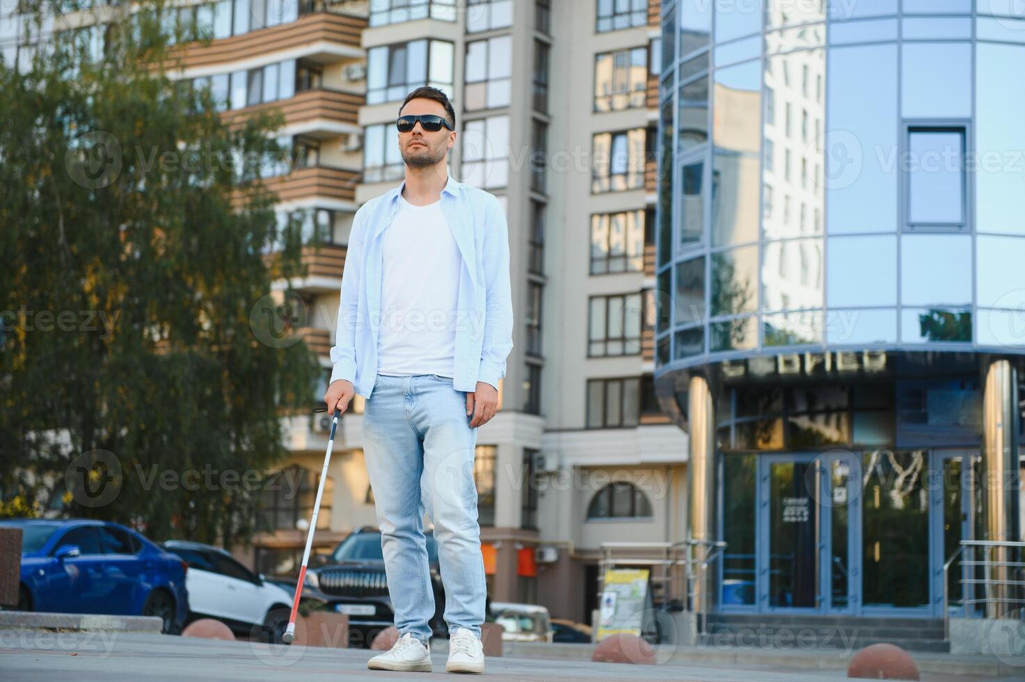 Young handsome blinded man walking with stick in town photo