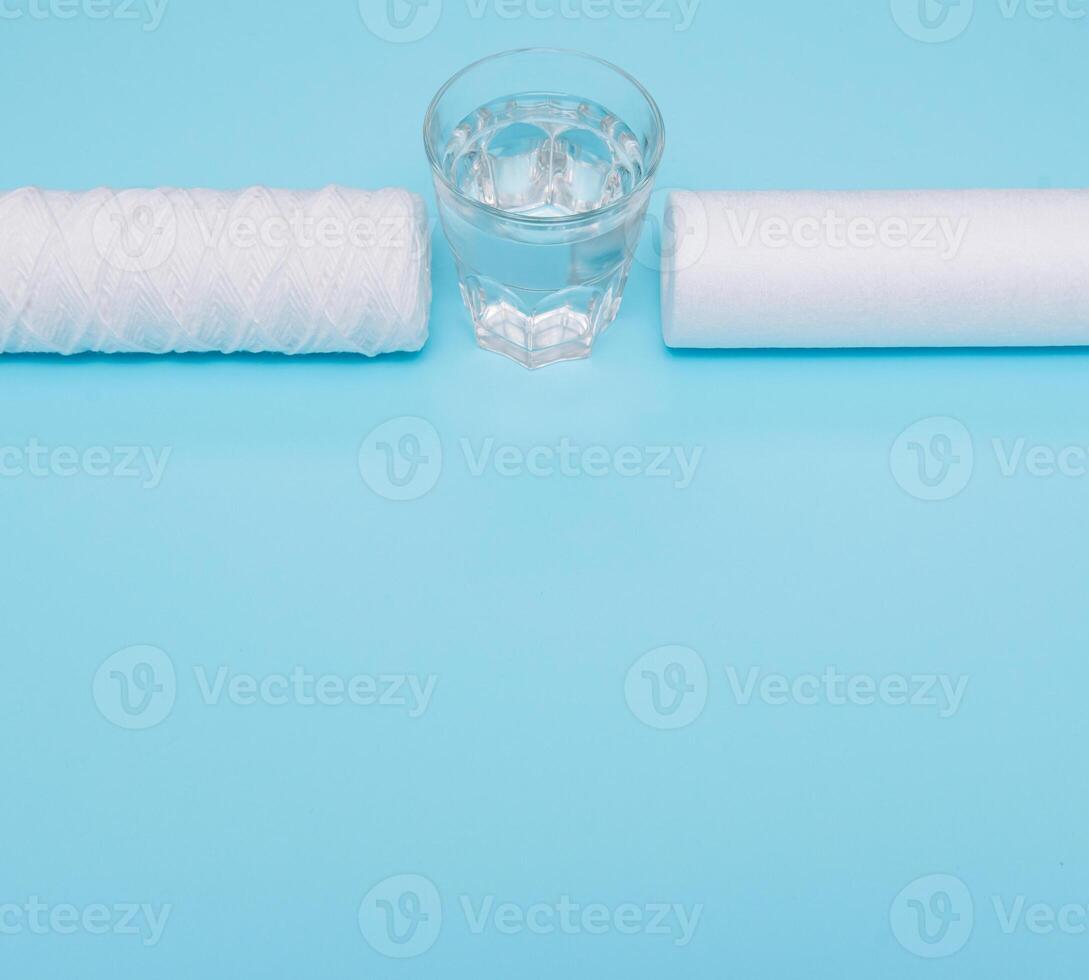 Water filters. Carbon cartridges and a glass with water on a blue background. Household filtration system photo