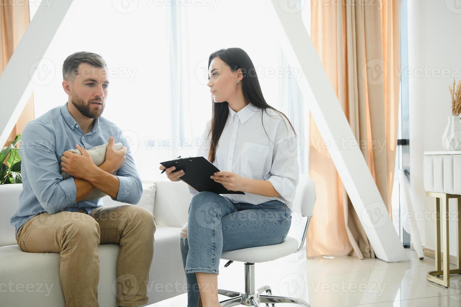 Session with a psychologist, psychotherapist. Young depressed male patient and professional female doctor with note pad. Lifestyle. Mental health care. photo