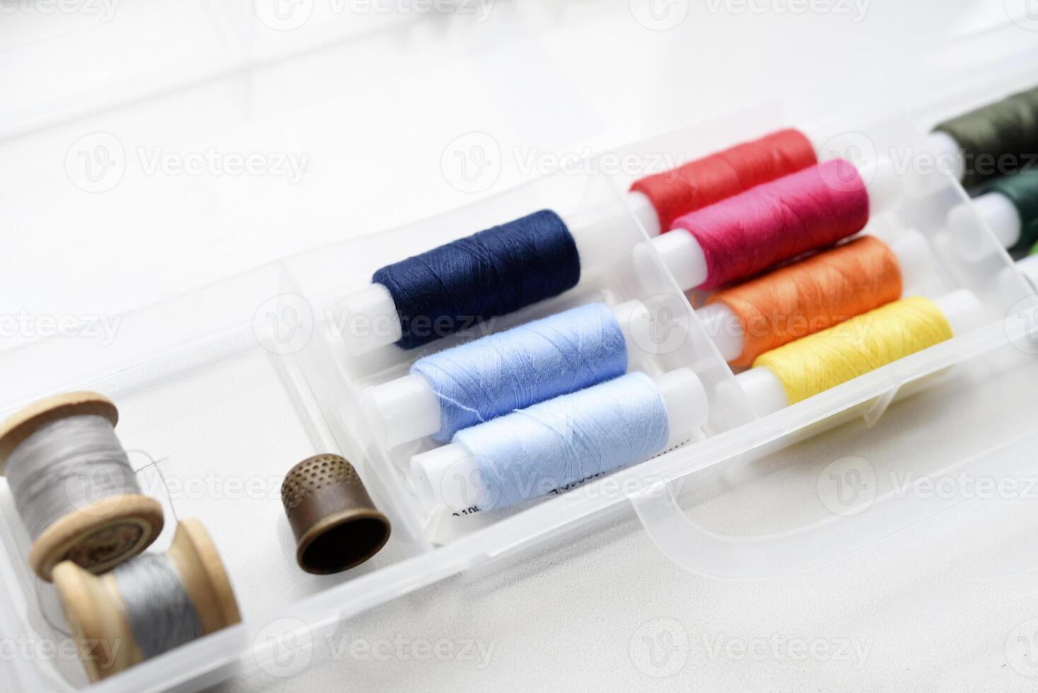 Multicolored skeins of thread in the set. Threads and a thimble in a plastic box. photo