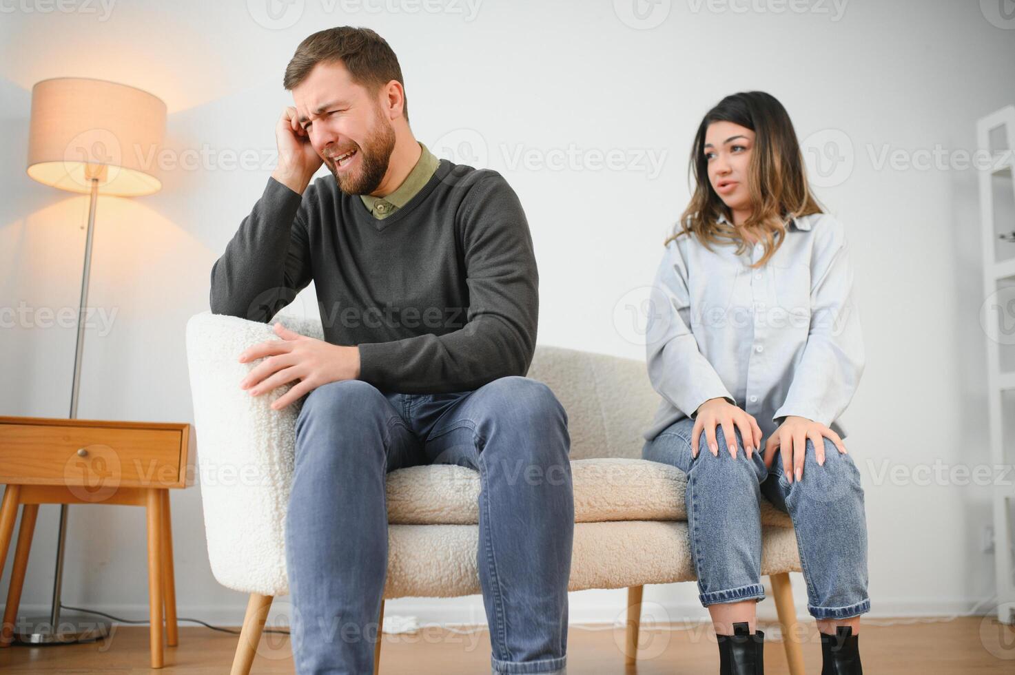 Couple arguing. Wife shouting to her desperate husband sitting on a couch in the living room at home photo