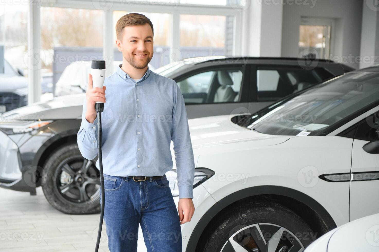 joven hombre, de venta eléctrico carros en el sala de exposición. concepto de comprando Respetuoso del medio ambiente coche para familia foto