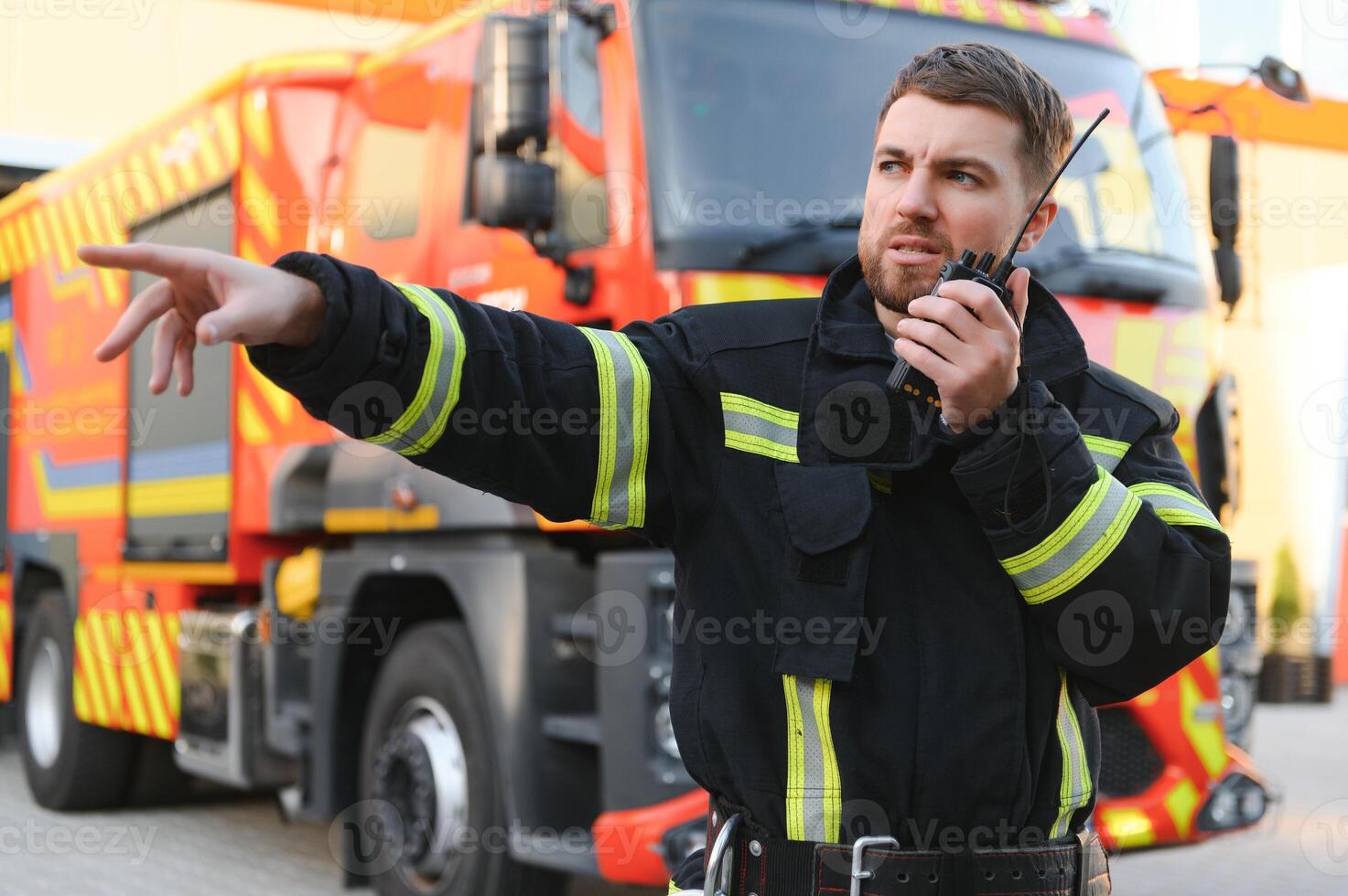 Firefighter in uniform using portable radio set near fire truck outdoors photo