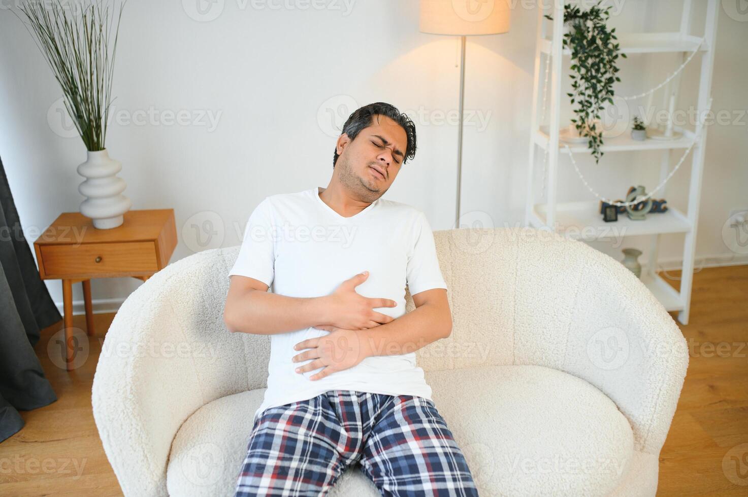 Sad exhausted guy of indian and arabian ethnicity, holds his hands on his stomach, grimaces from pain in his stomach, suffers from poisoning, spasm, stomach problems photo