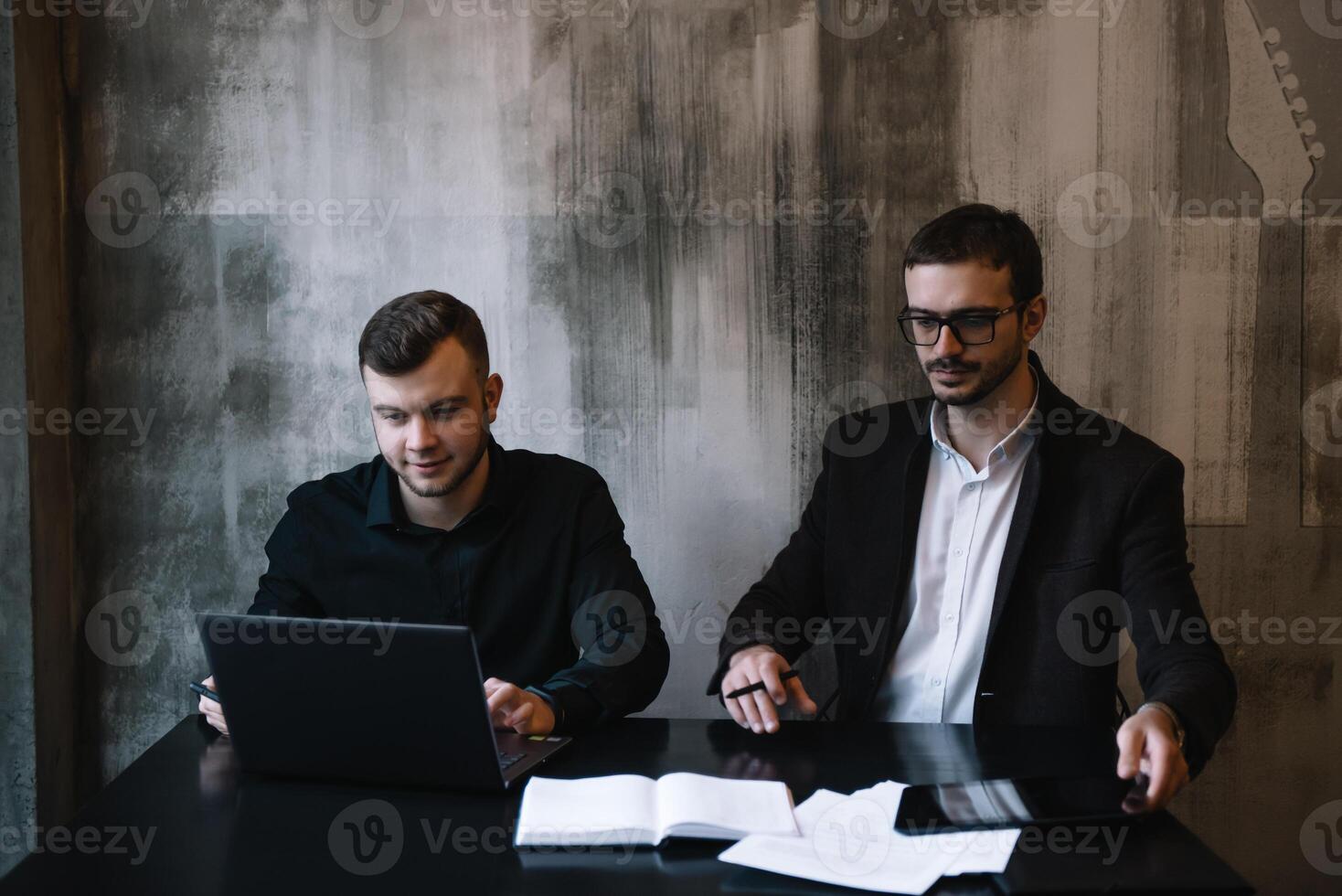 dos empresarios en un oficina sonriente a el cámara mientras trabajando juntos detrás un ordenador portátil computadora. foto