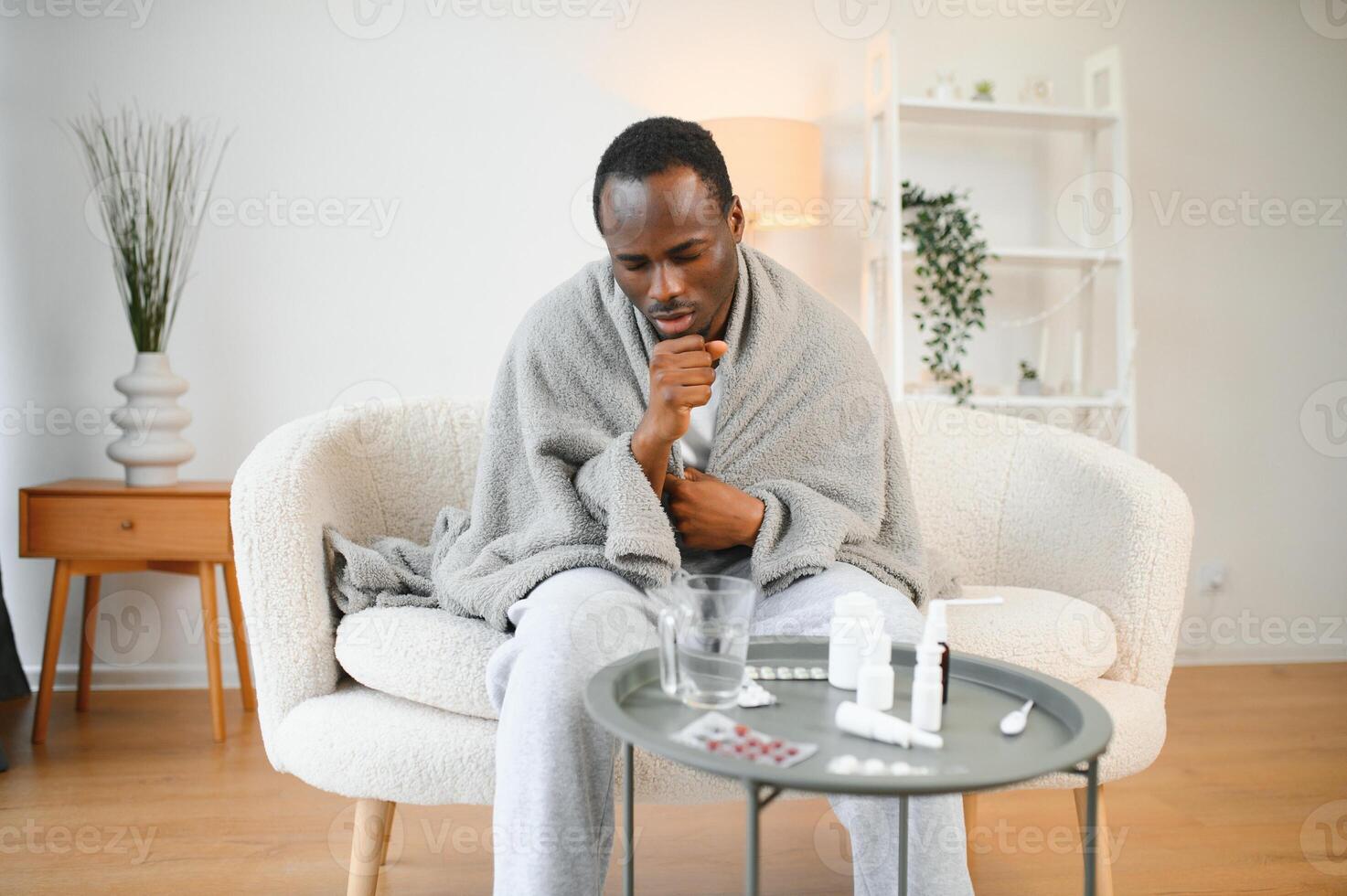 Portrait of a sick young african american man wrapped in a blanket on the sofa. Guy with seasonal flu or cold feel unhealthy with influenza and runny nose at home photo