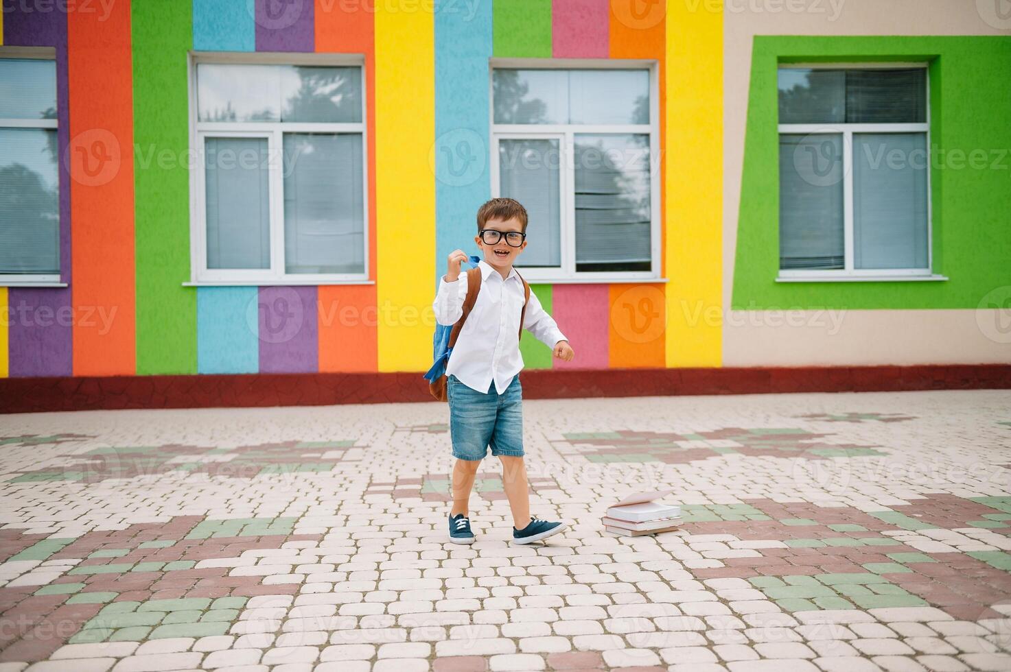 Back to school. Happy smiling boy in glasses is going to school for the first time. Child with backpack and book outdoors. Beginning of lessons. First day of fall photo