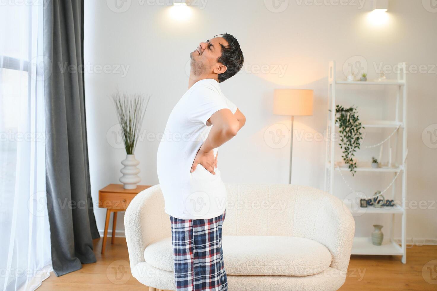 Portrait of Indian guy backache, holding spine with hand photo