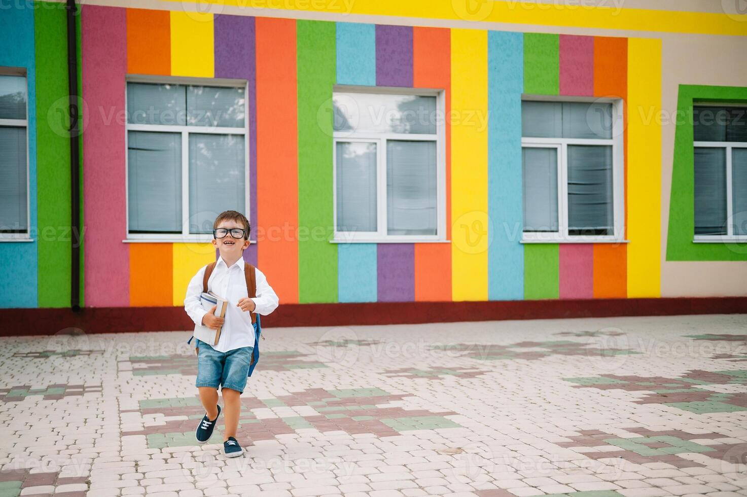 Back to school. Happy smiling boy in glasses is going to school for the first time. Child with backpack and book outdoors. Beginning of lessons. First day of fall. photo