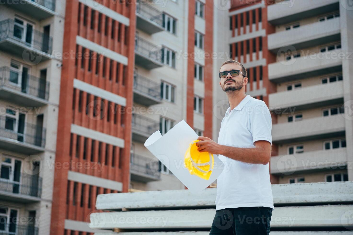 Portrait of an architect builder studying layout plan of the rooms, serious civil engineer working with documents on construction site. photo