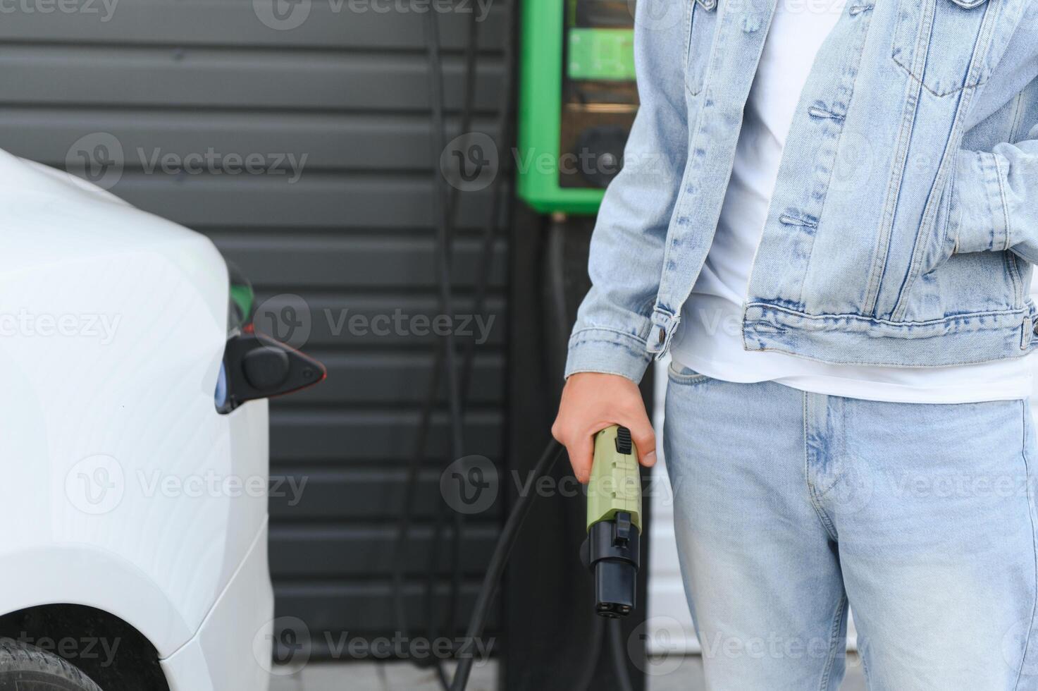 young handsome man holding charging cable at electric charging station point standing near his new car photo