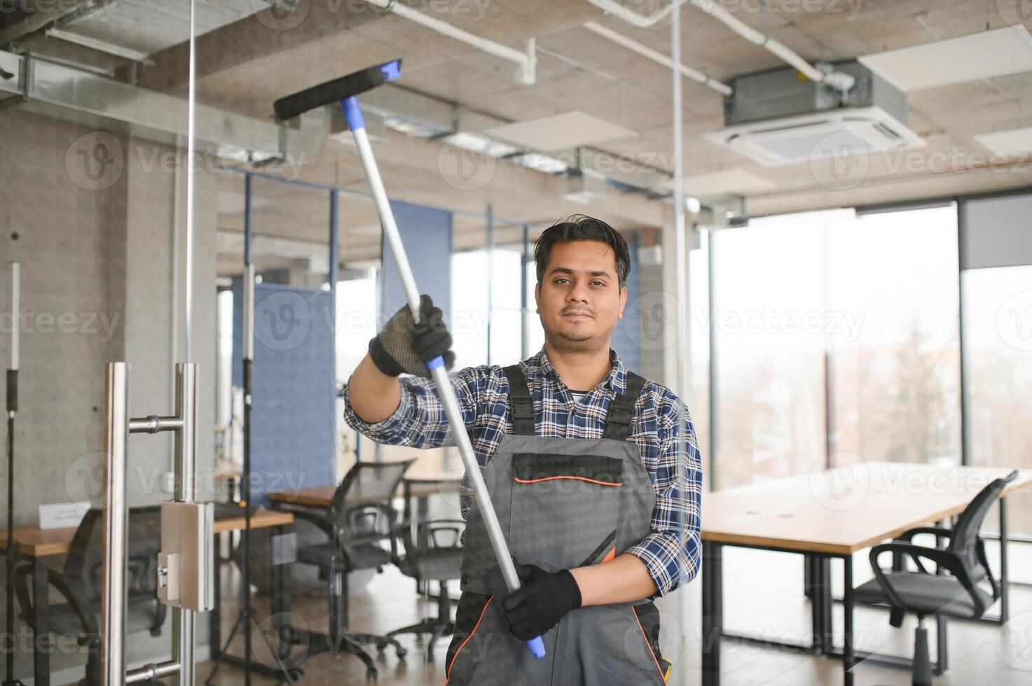 Male professional cleaning service worker in overalls cleans the windows and shop windows photo