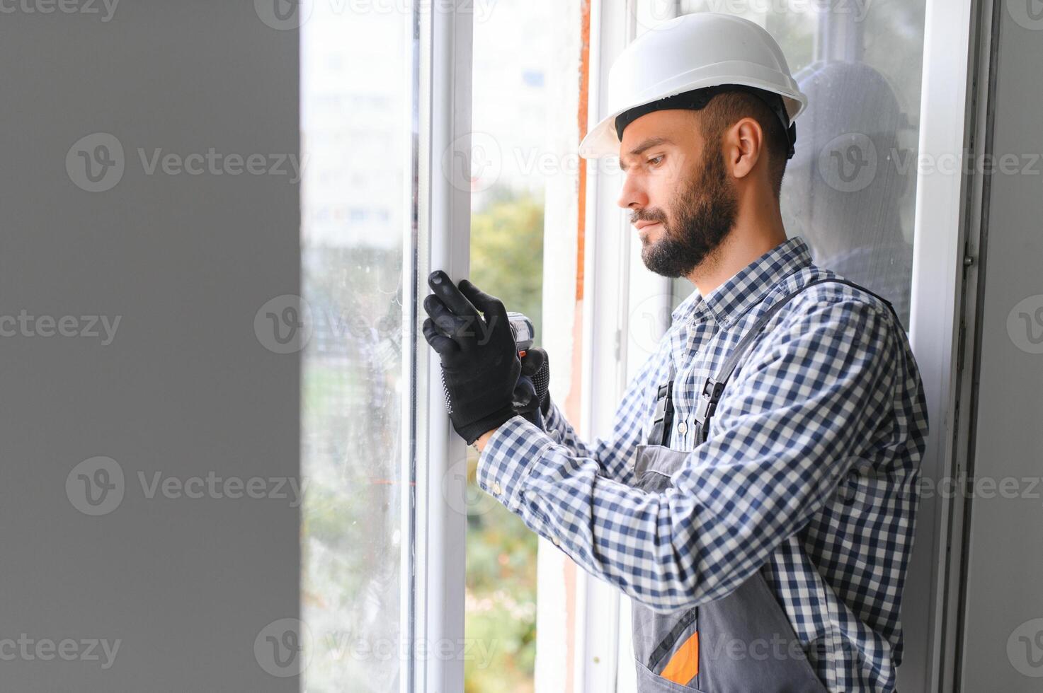 obrero en mono instalando o ajustando el plastico ventanas en el vivo habitación a hogar foto