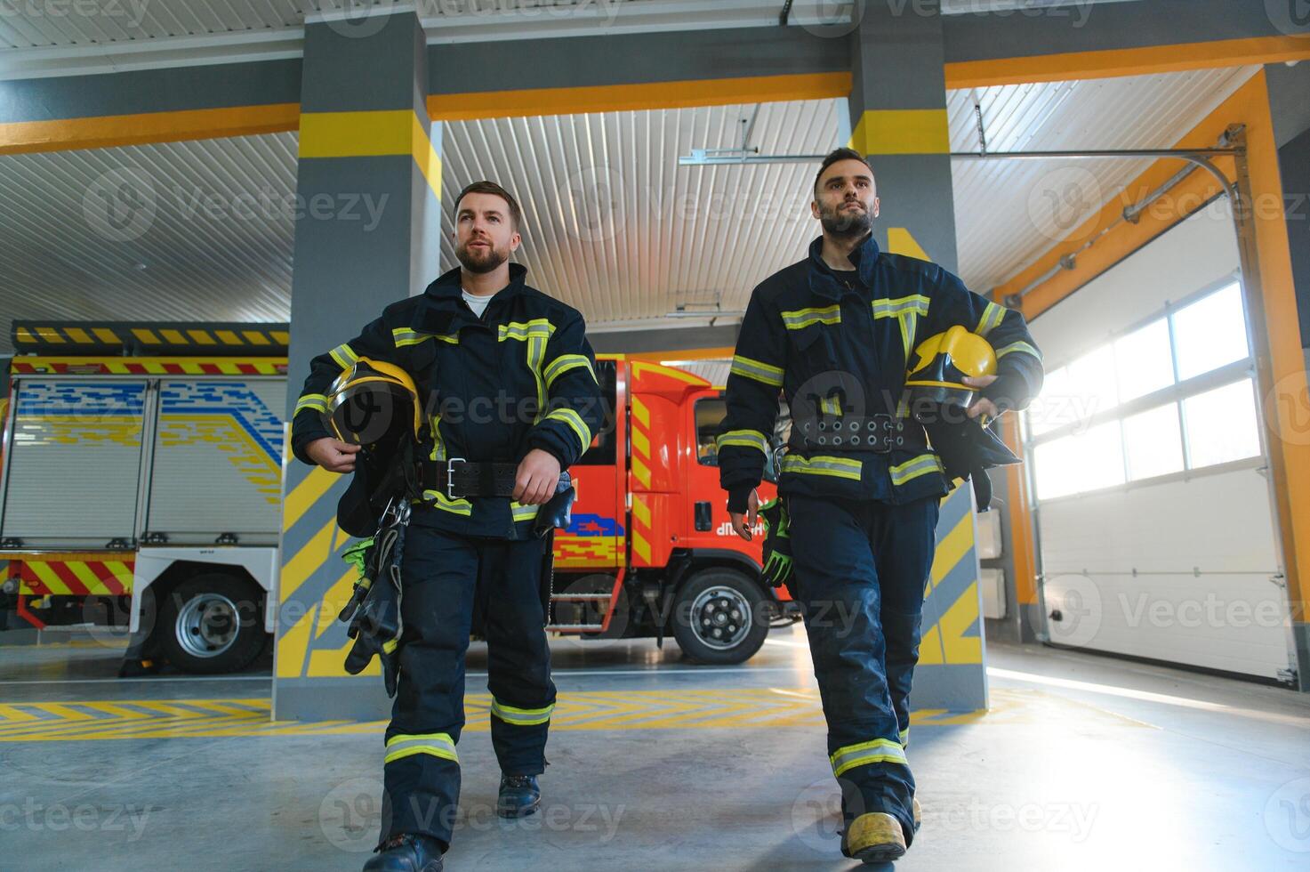 Two firefighters in protective clothing in helmets with fire engine photo